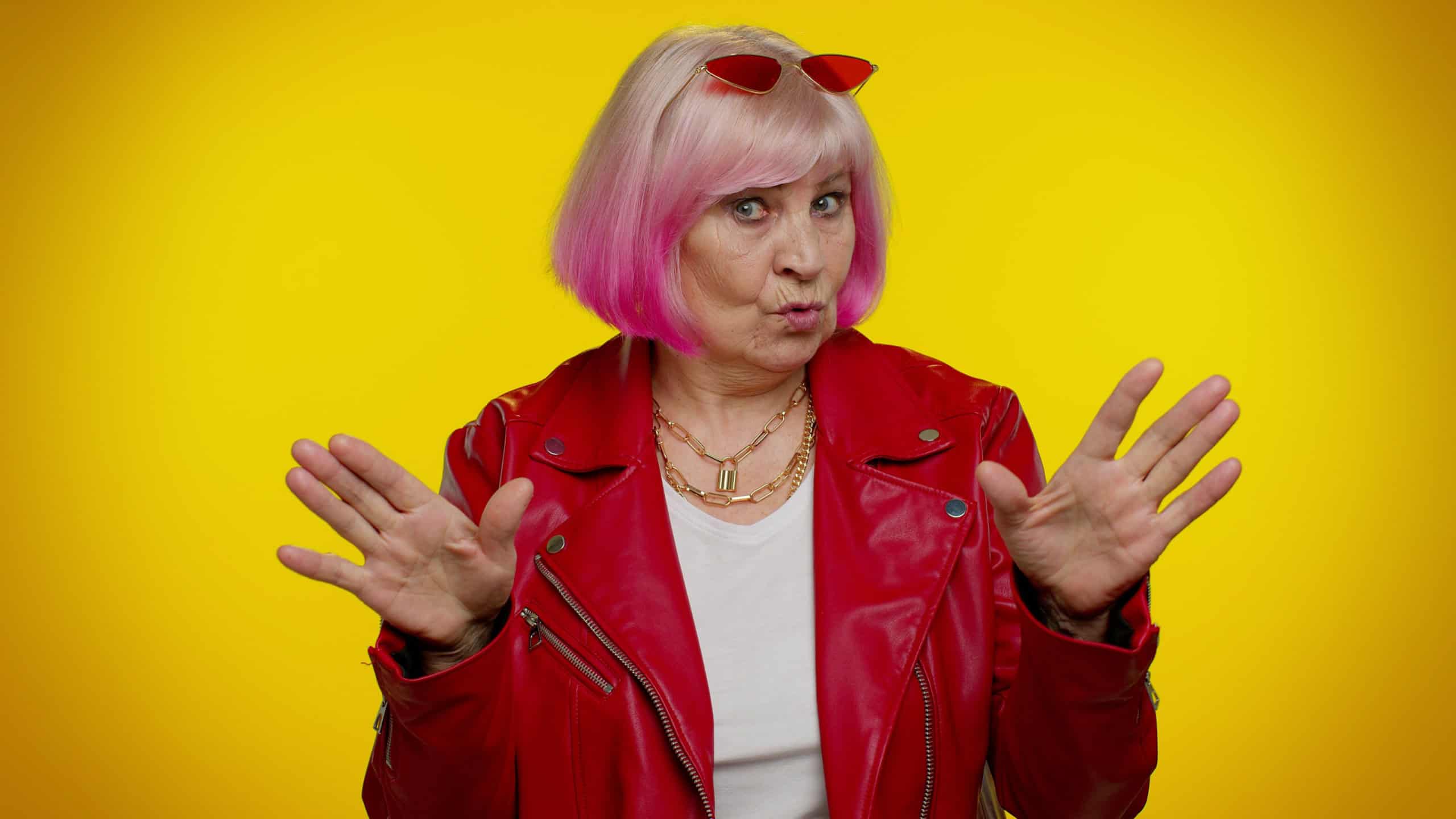I am not guilty. Confused senior old granny woman with pink hair pointing fingers himself ask say who me no thanks i do not need it isolated on yellow studio background. Elderly grandmother pensioner