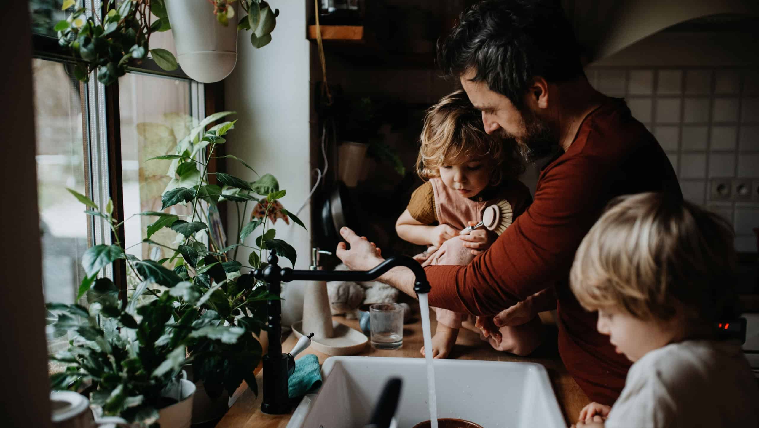 Mature father with two small children washing dishes indoors at home, daily chores concept.