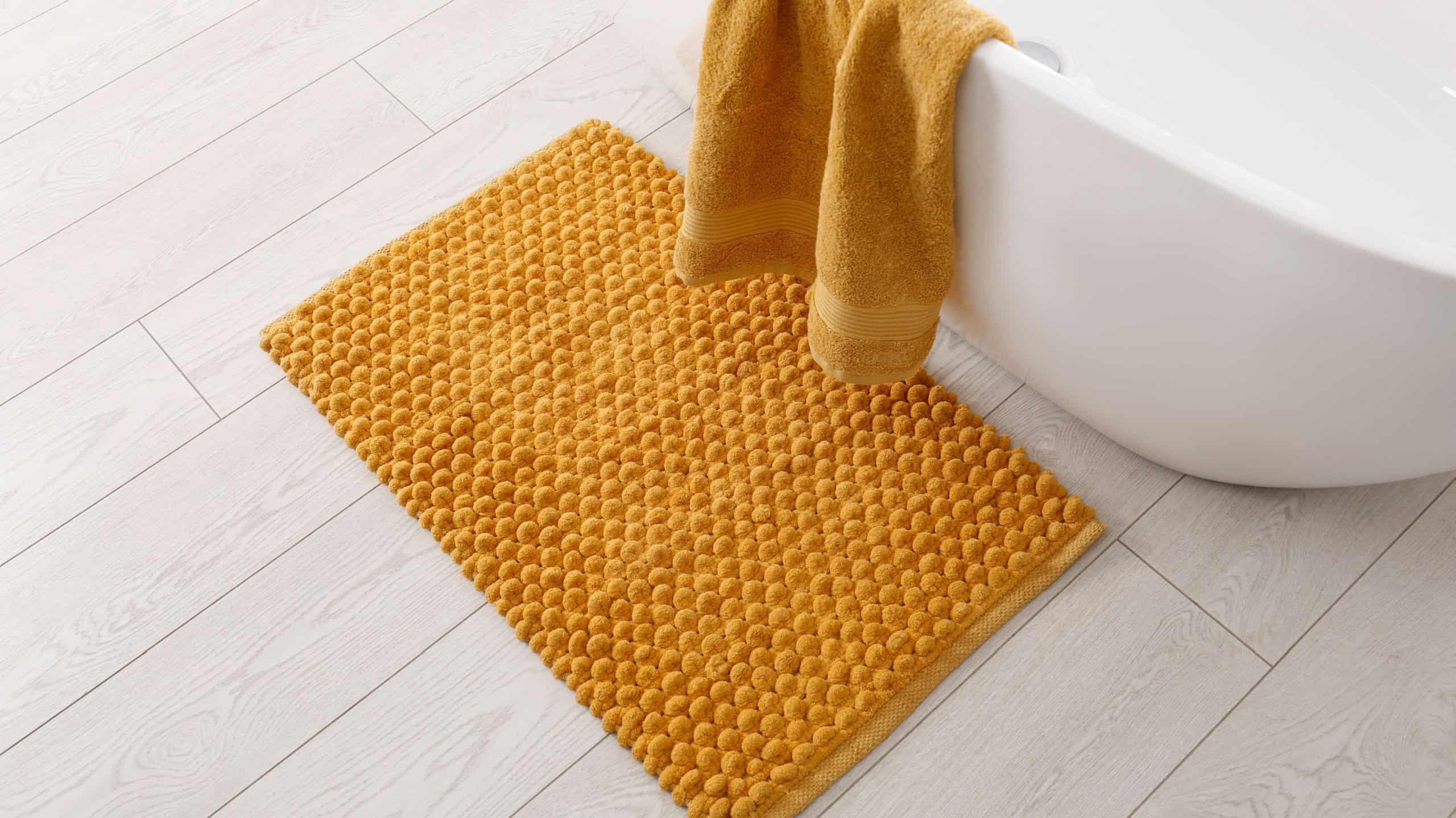 Soft orange bath mat on floor in bathroom