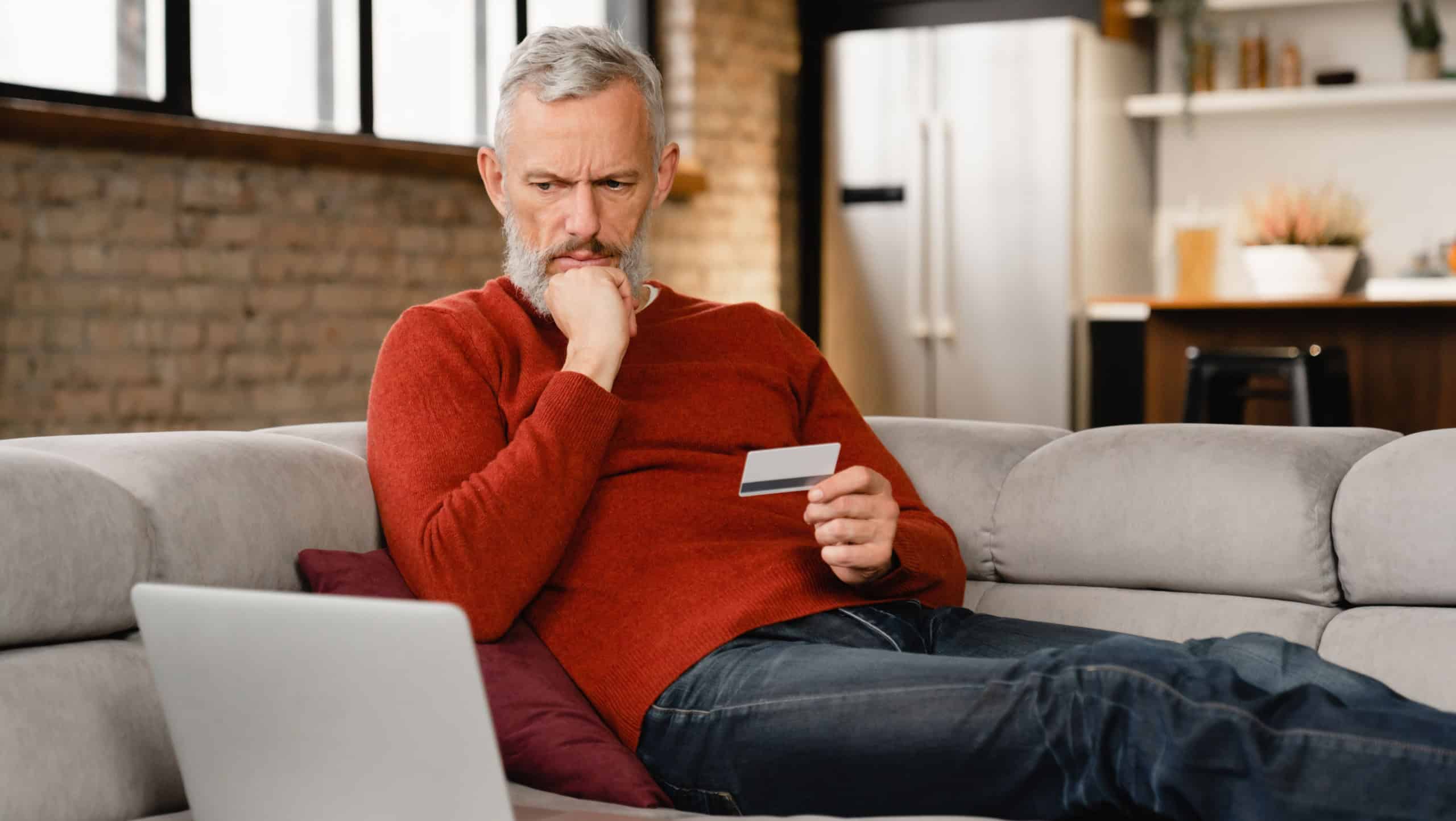Serious caucasian mature middle-aged man doing shopping online, buying purchasing presents clothes remotely, ordering food delivery with credit card e-commerce banking on laptop at home