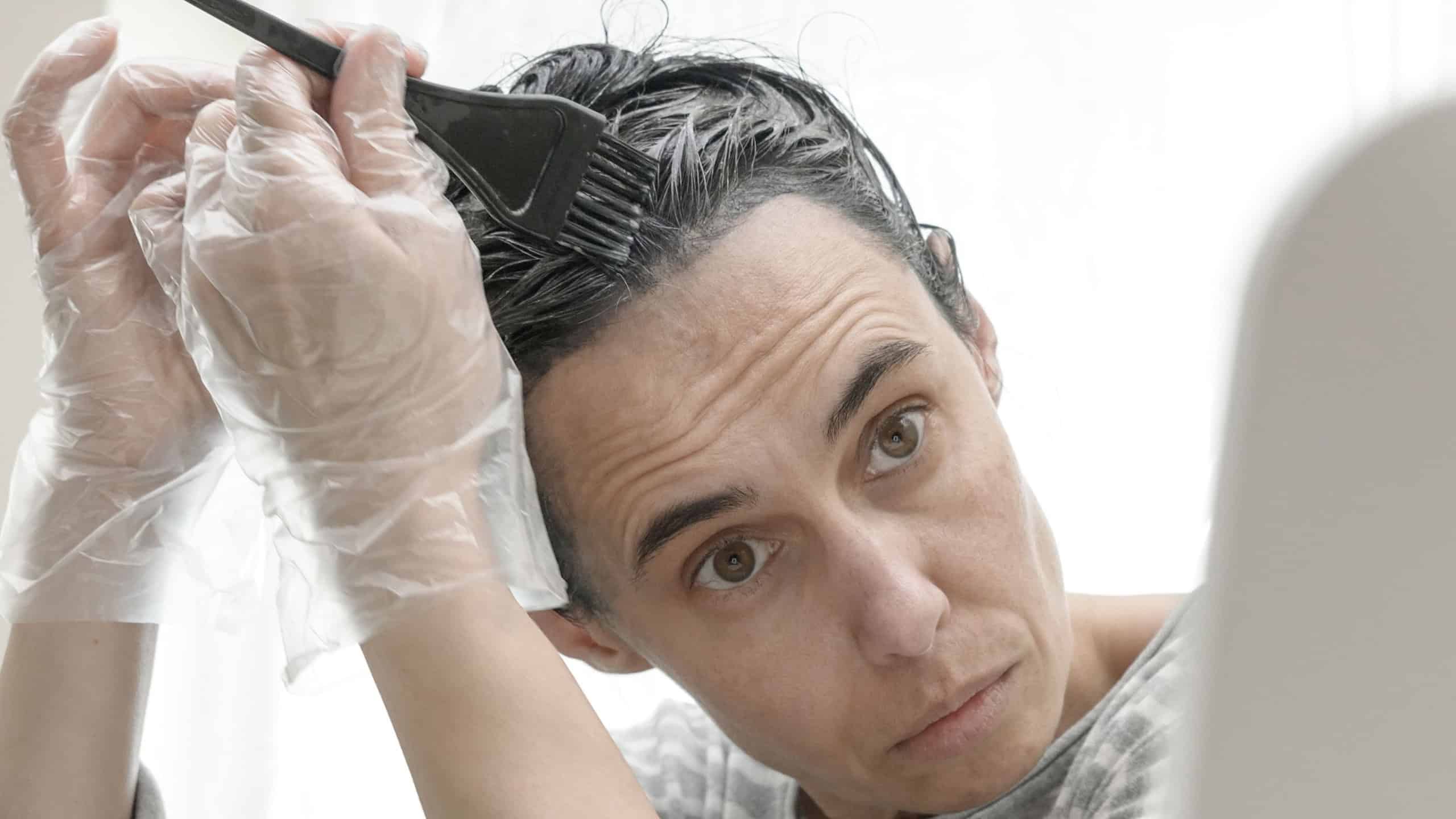 Closeup woman dyeing hair. Middle age woman colouring dark hair with gray roots at home