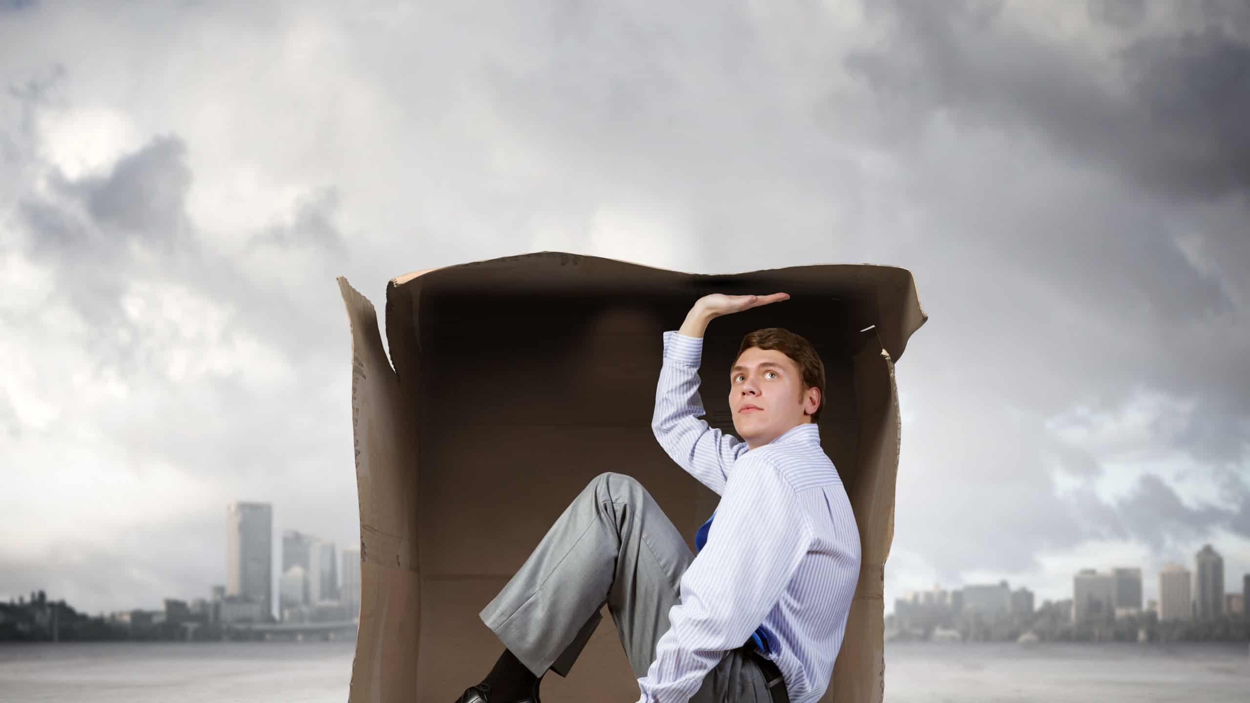 Young frustrated businessman trapped in small carton box