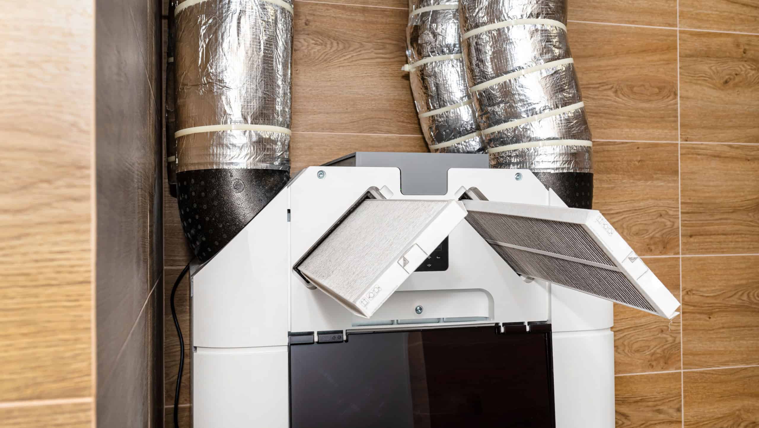 Home mechanical ventilation with heat recovery hanging on the wall, visible dirty filters sticking out of the device.