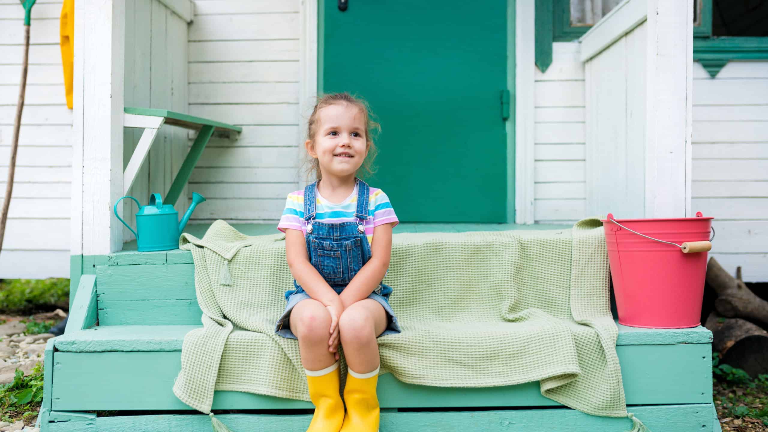 Life in the suburbs. Cute girl sitting on porch at backyard against house. Kids relaxing on steps. Summertime and childhood concept.