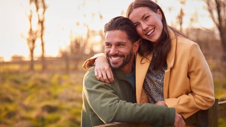 Loving Couple On Walk Through Autumn Countryside Resting On Fence Together