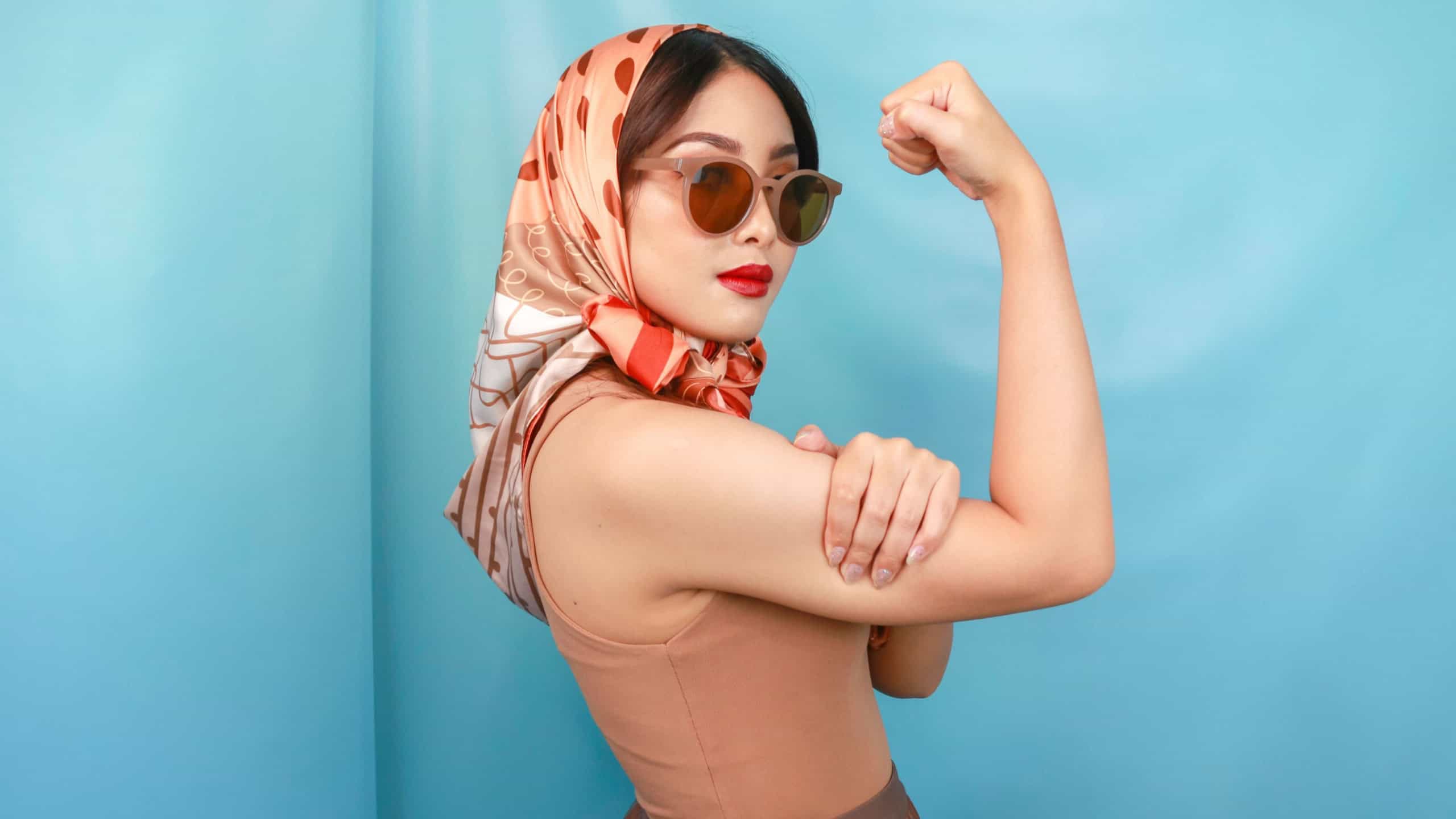Retro concept of a young Asian strong woman showing her biceps isolated by a blue background