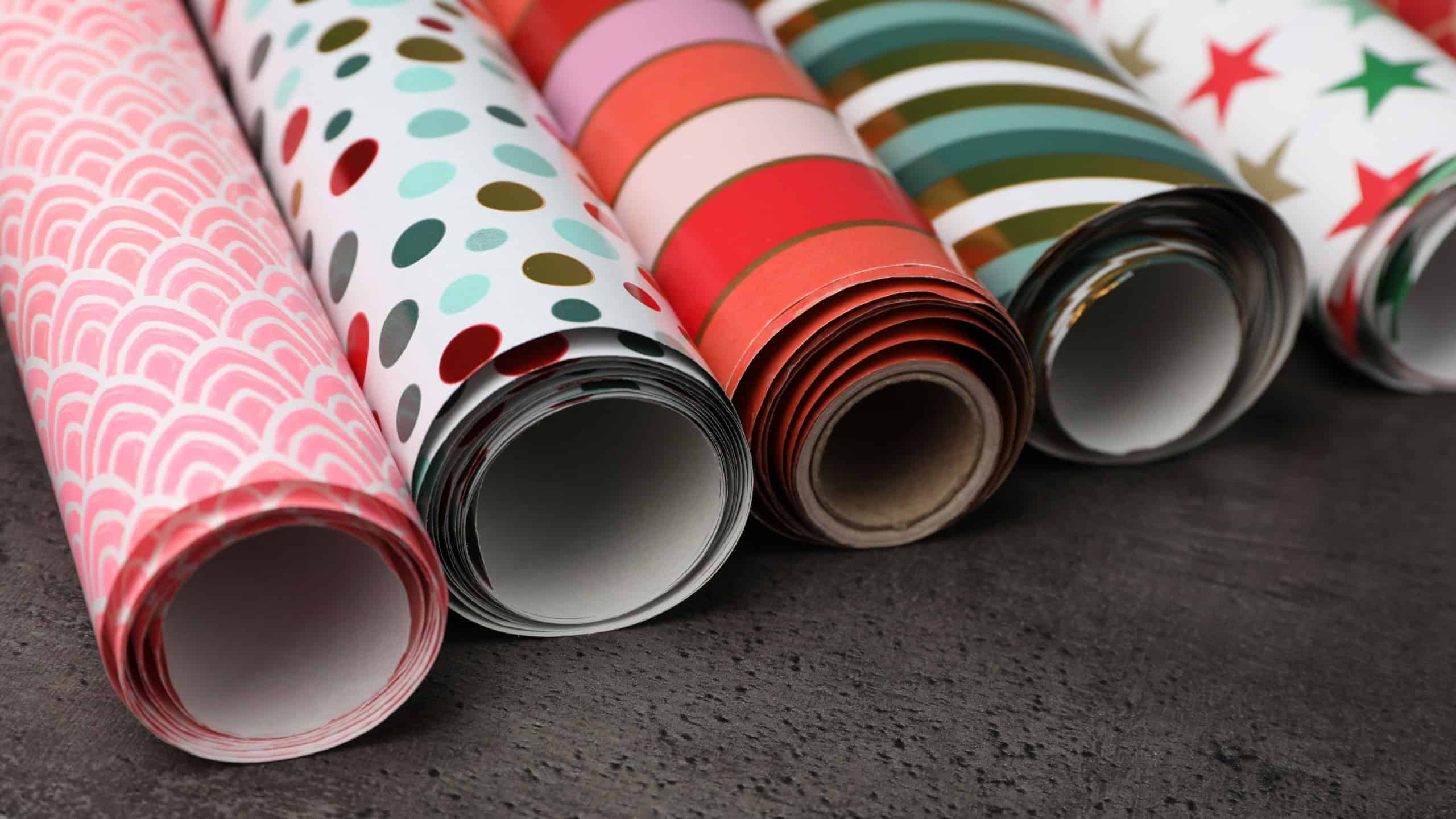 Different colorful wrapping paper rolls on grey table, closeup