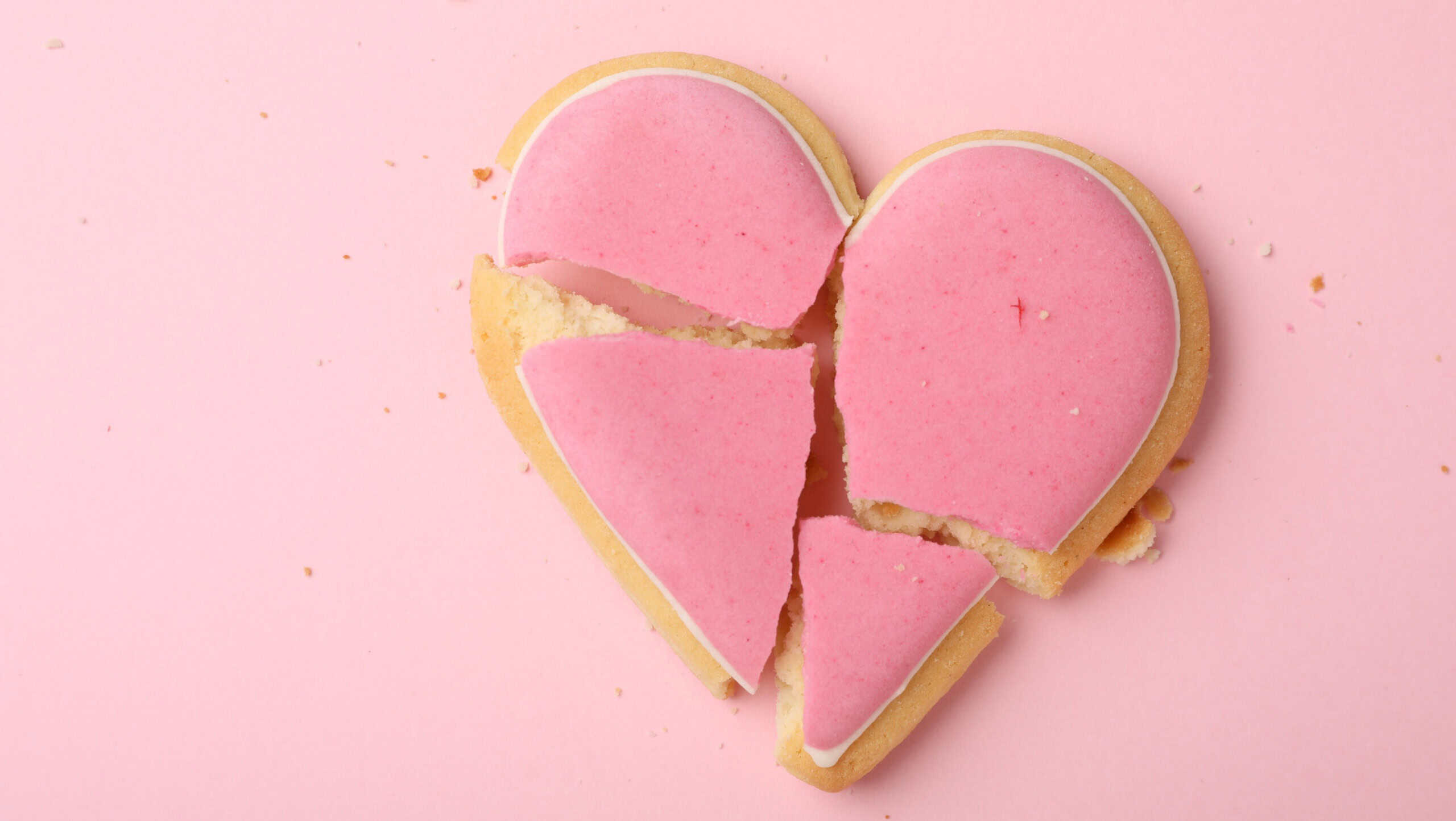 Broken heart shaped cookie on pink background, top view. Relationship problems concept