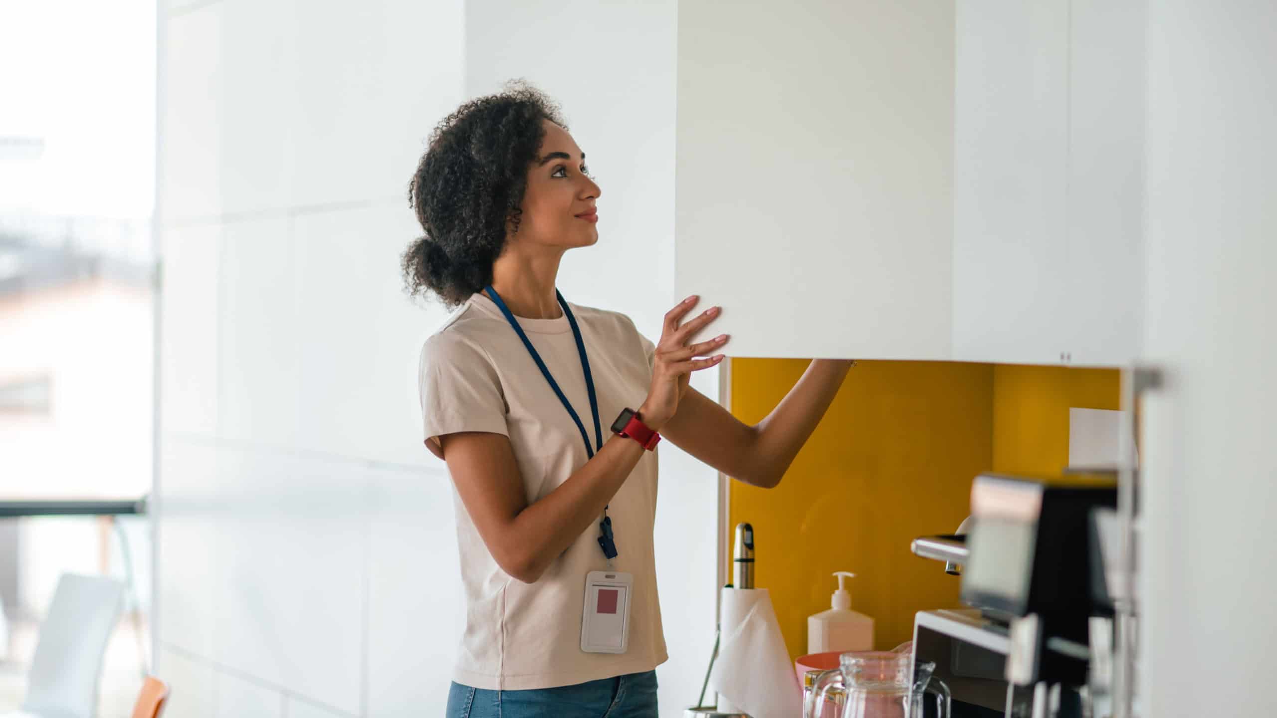 Office worker in the office kitchen taking something from the cupboard