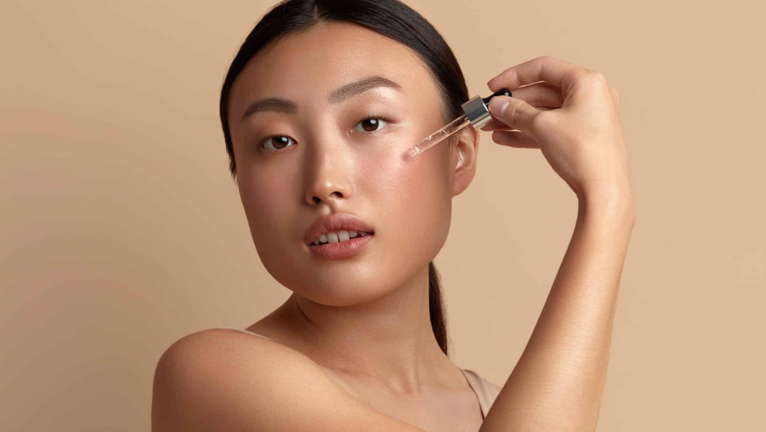 Woman Applying Serum on Face. Woman Applying Essential Oil On Facial Skin And Looking at Camera. Beautiful Model Moisturizing Derma With Natural Vitamin E, Serum Collagen And Hyaluronic Acid
