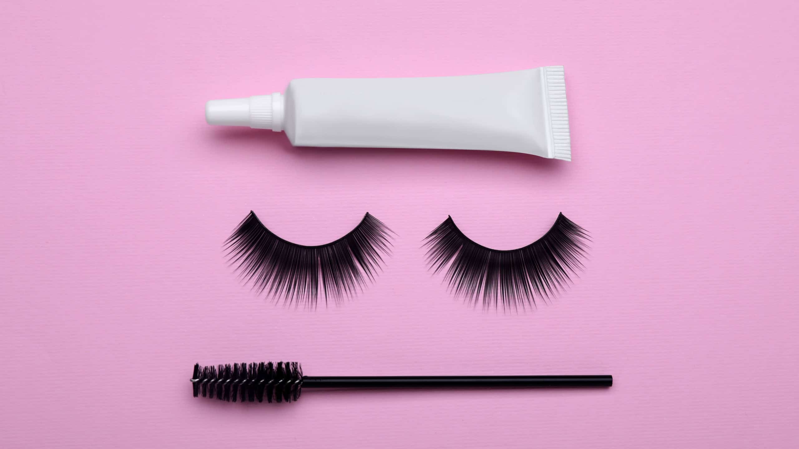 Flat lay composition with fake eyelashes on pink background