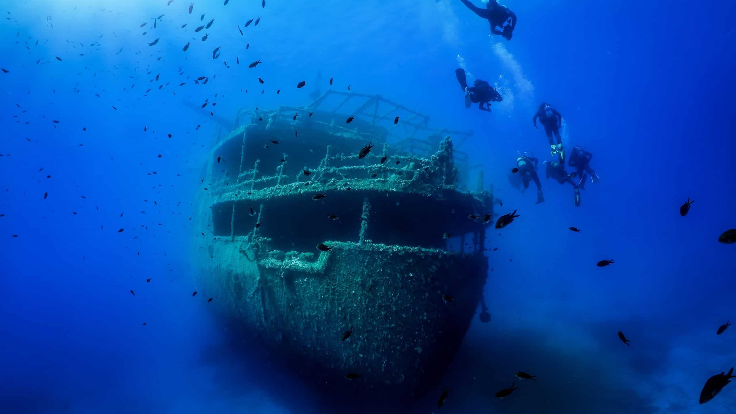 A group of unrecognizable divers explore a sunken shipwreck in the blue, mediterranean sea at Naxos island, Greece