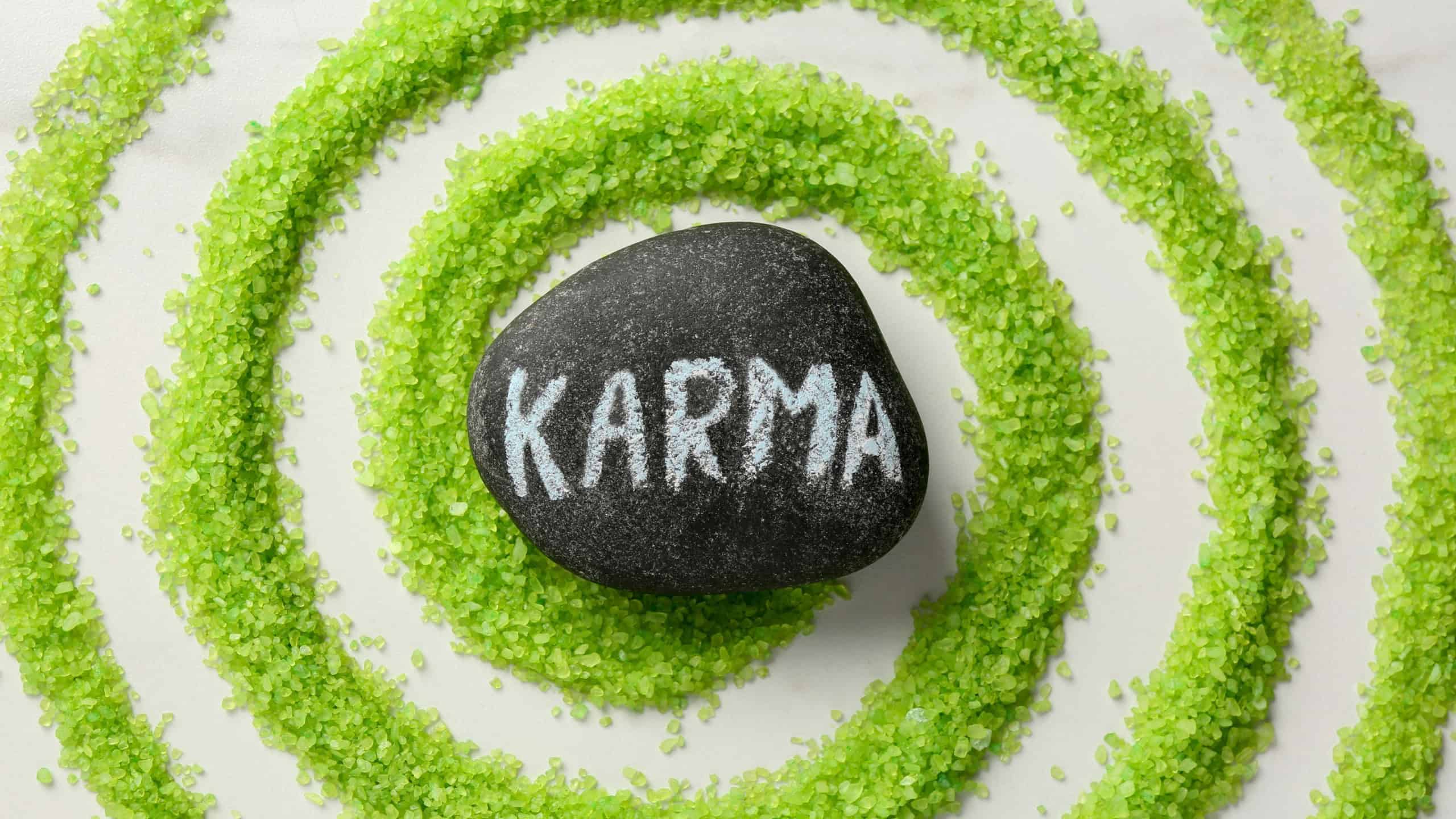 Stone with word Karma and circle made of light green sea salt on white marble table, top view