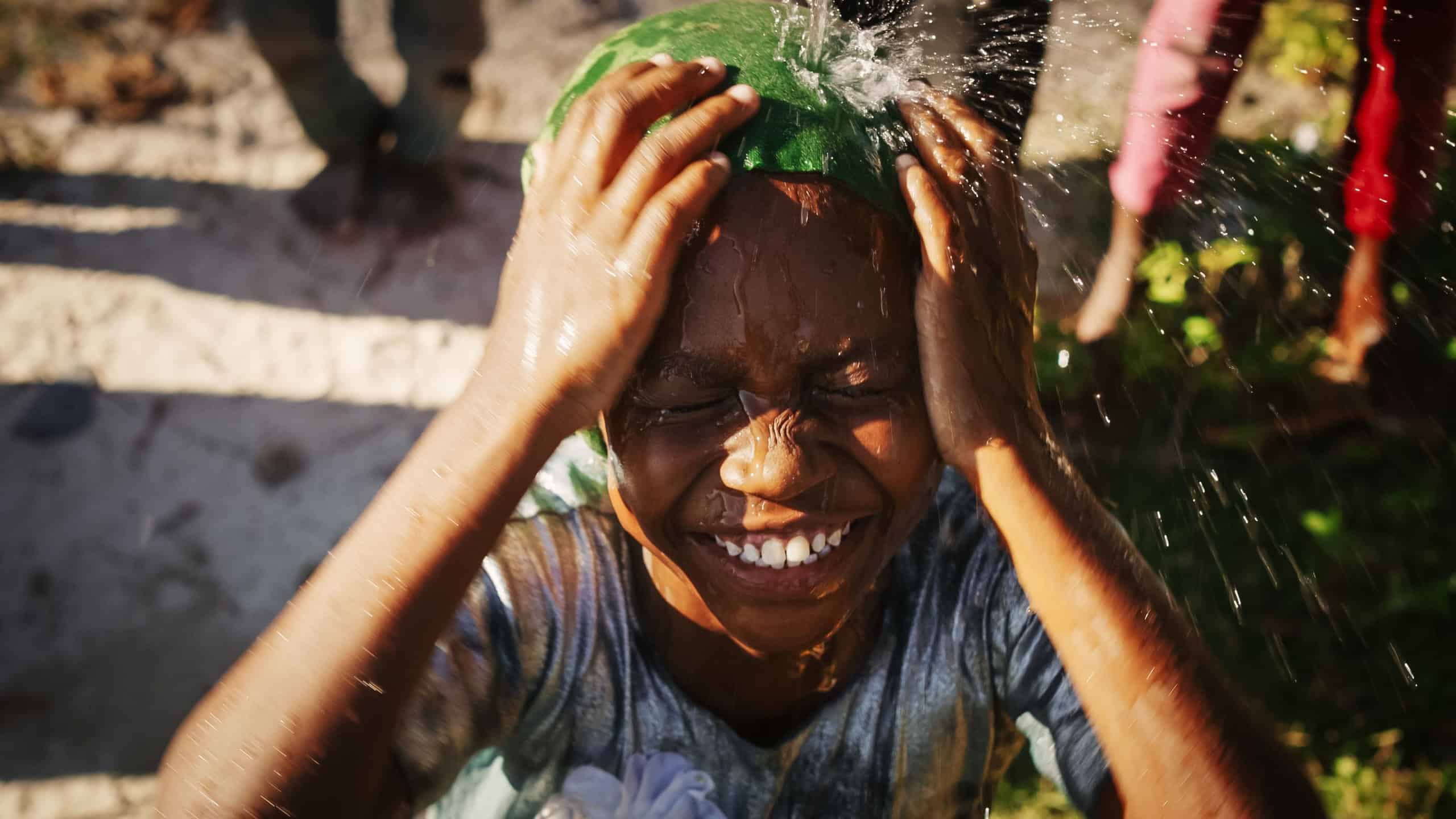 Portrait of African Little Girl Jumping and Dancing While Looking at the Camera Under Pouring Water.