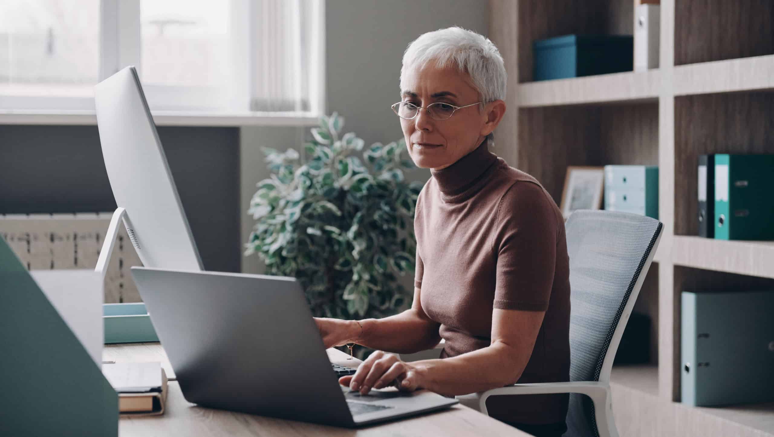 Confident senior businesswoman working at two computers while sitting in the office