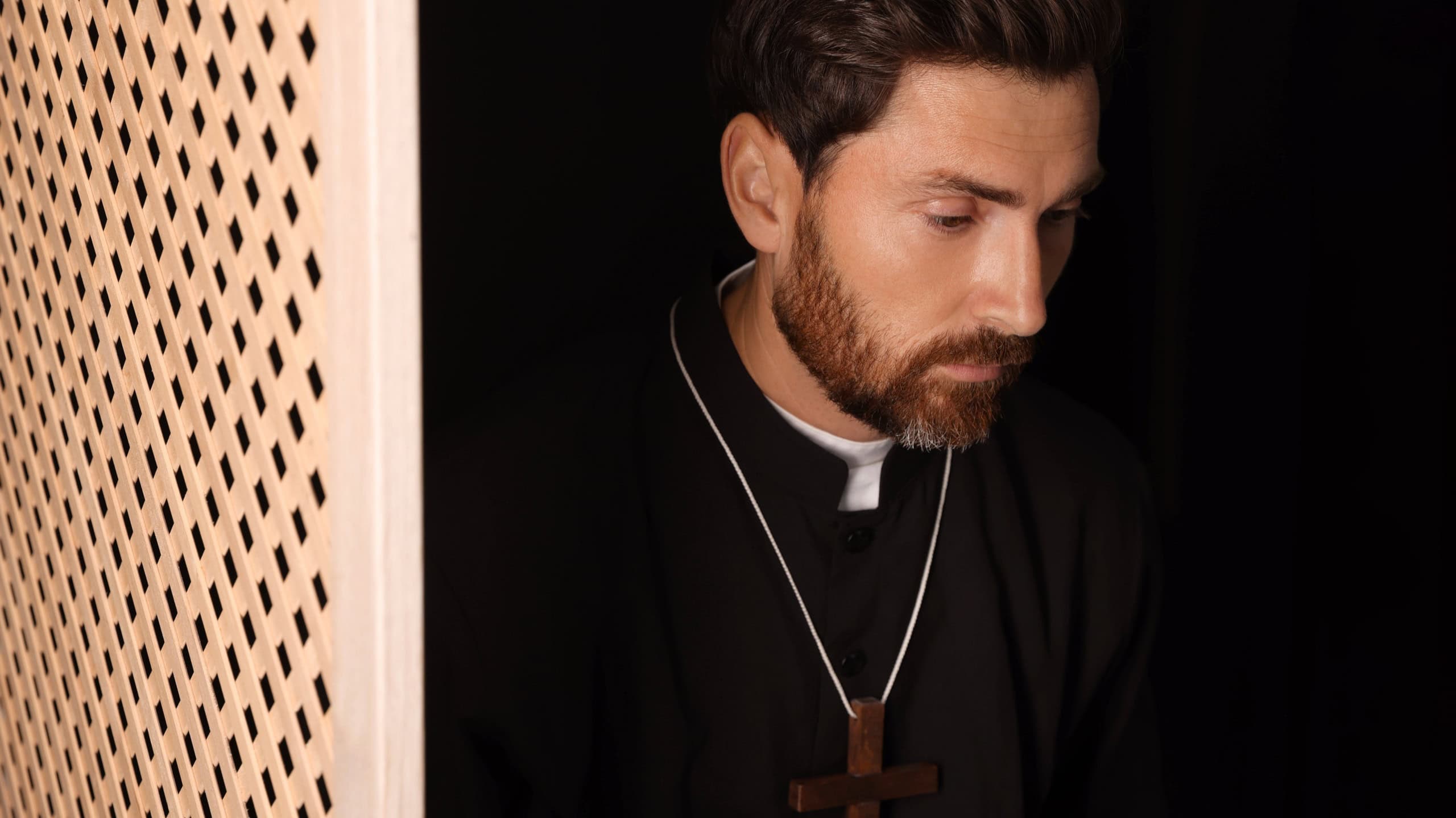 Catholic priest wearing cassock in confessional booth