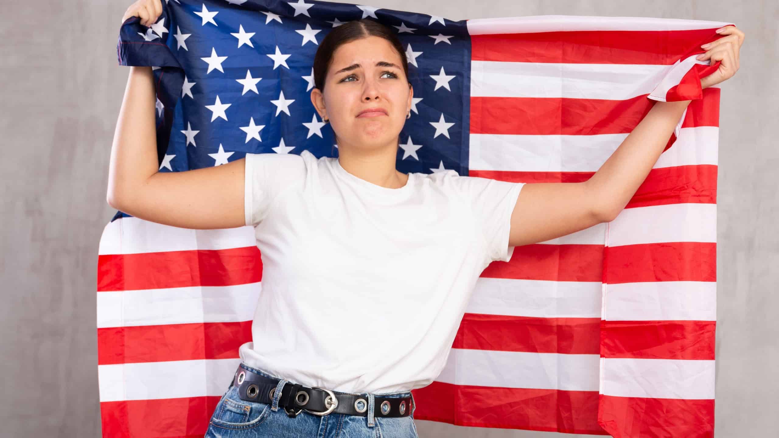 Frustrated girl with flag of United States of America flag in her hands.