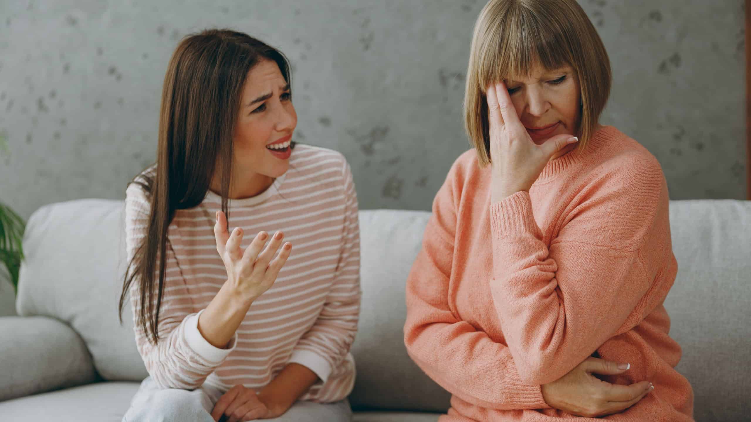 Two adult dissatisfied displeased women mature mom young kid wear casual clothes speak talk argue sit on gray sofa couch stay home flat rest relax spend free spare time in living room. Family concept