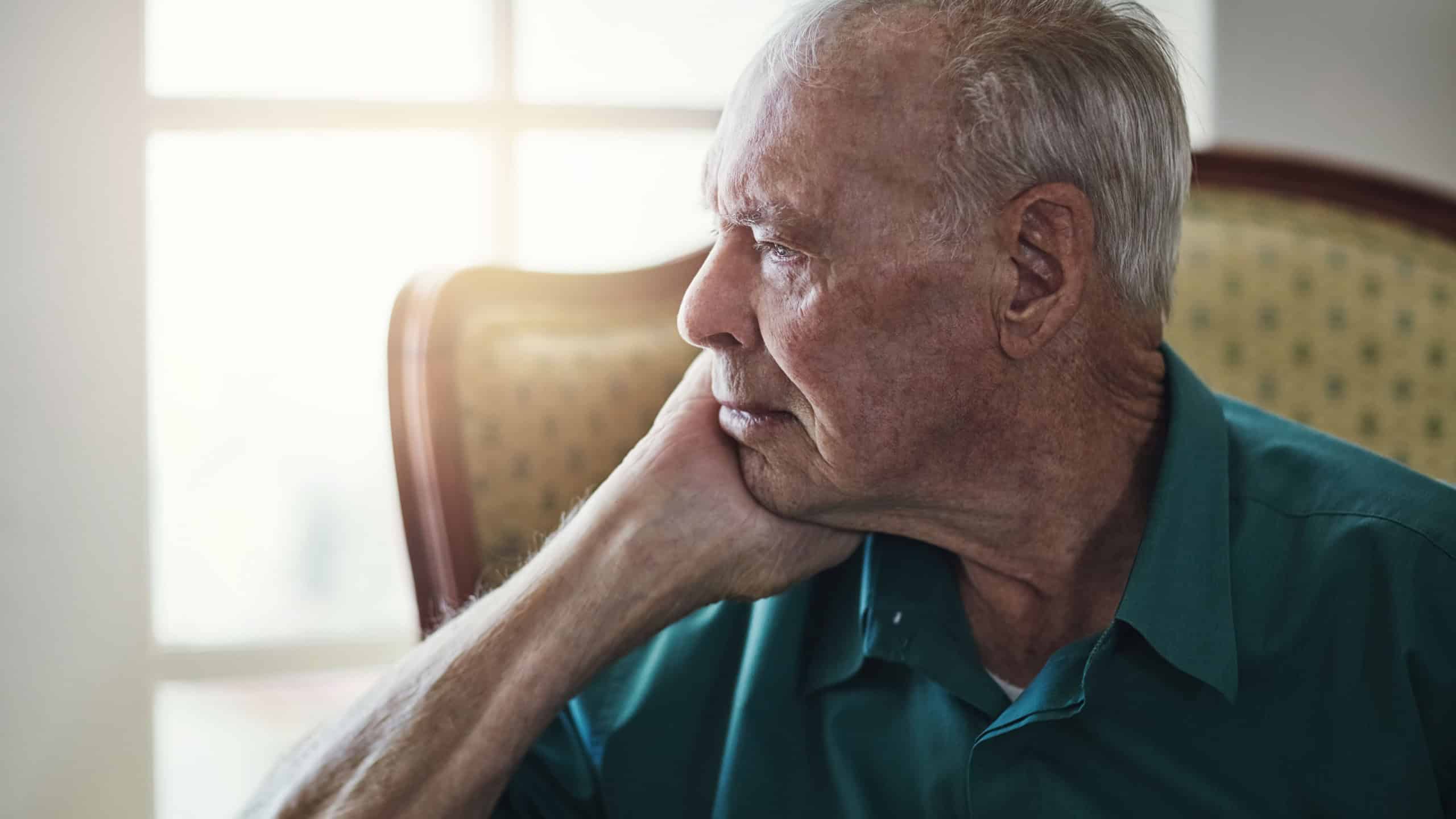 Senior man sitting by himself in a living room and looking sad