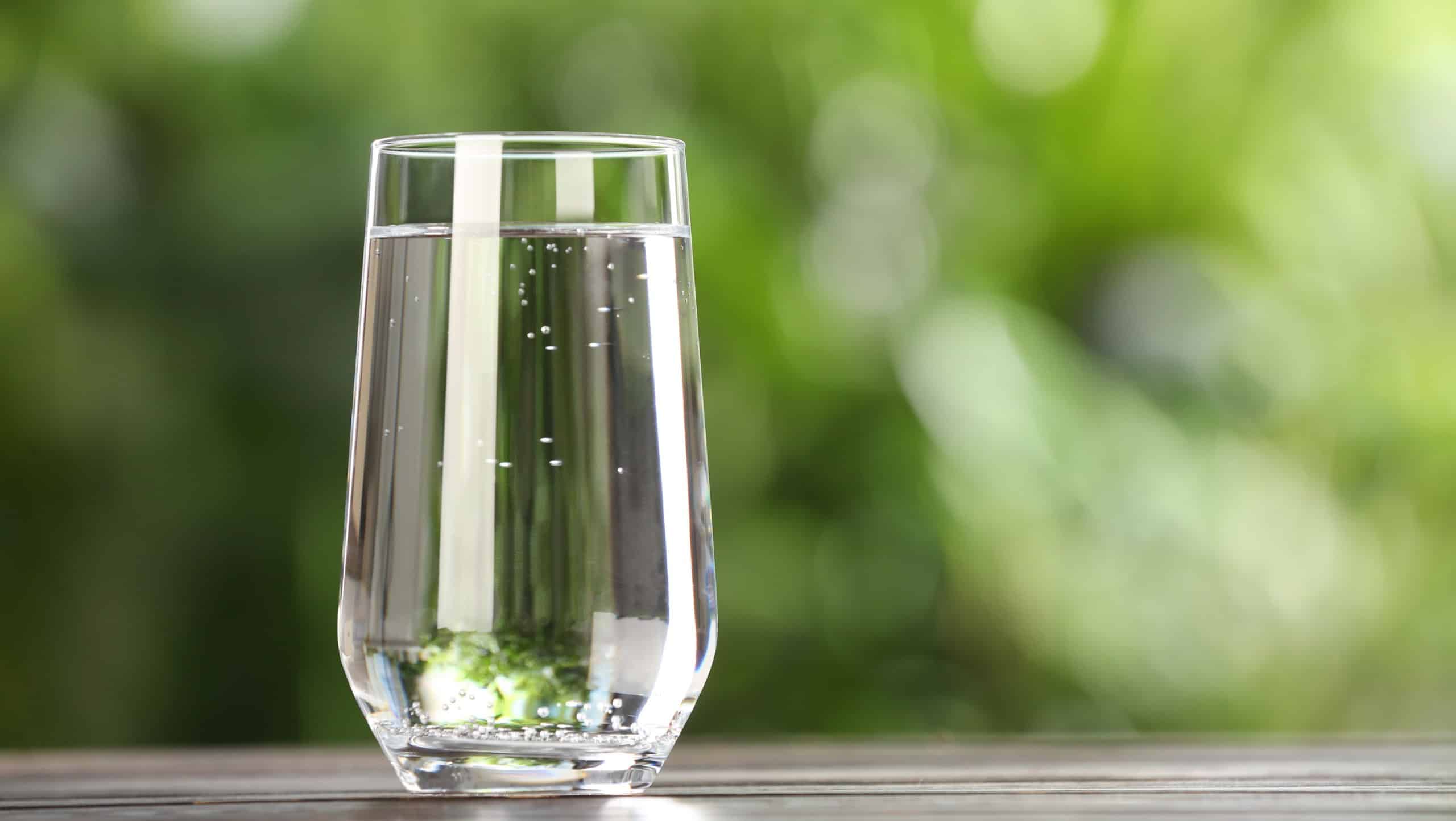 Glass of fresh water on wooden table outdoors. Space for text