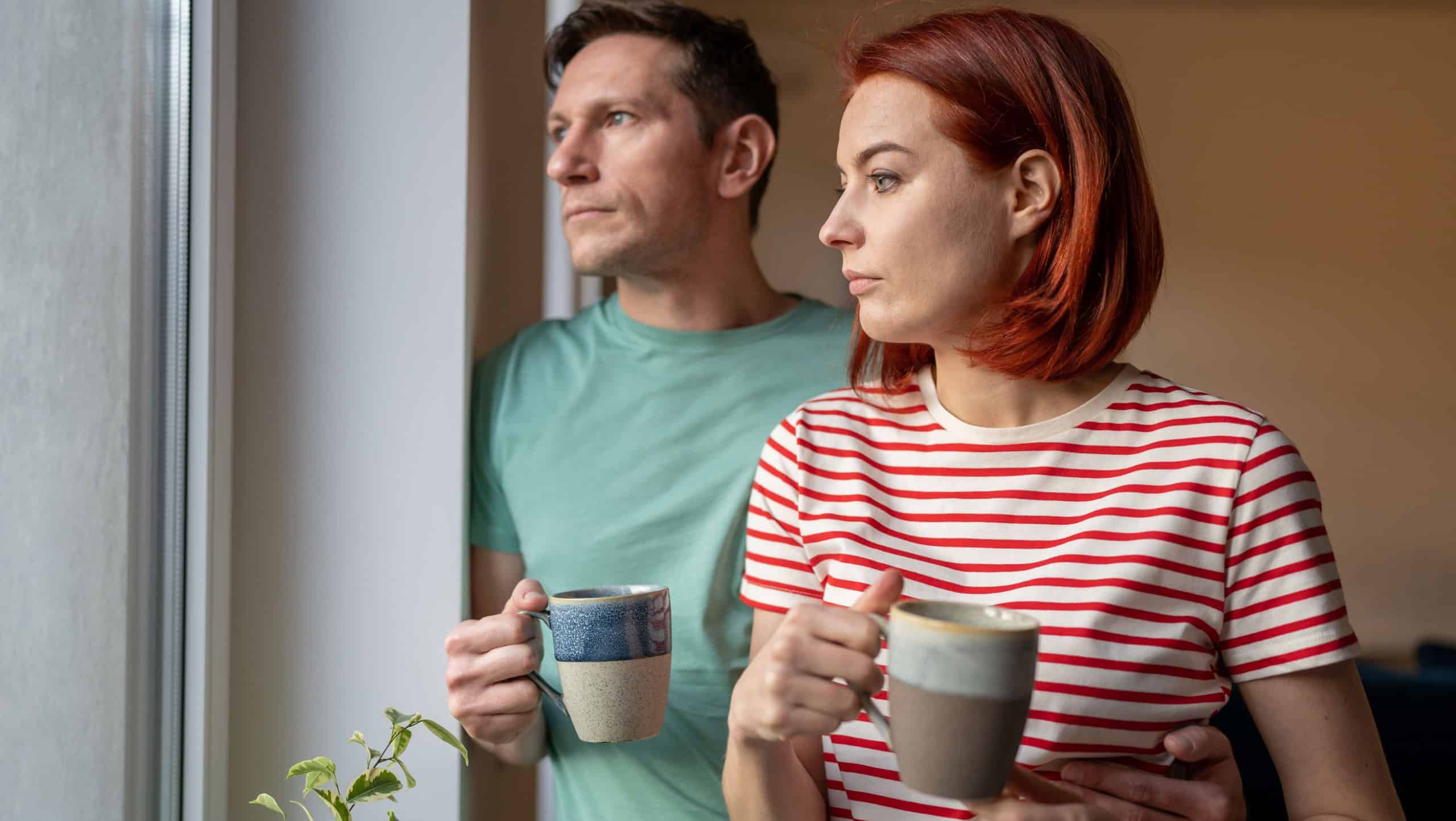 Upset girl and man hold cup of coffee, look out window, sad and anxious. Family problems. Unhappy husband and wife hustle about life and problem solving. Feelings loneliness in couple
