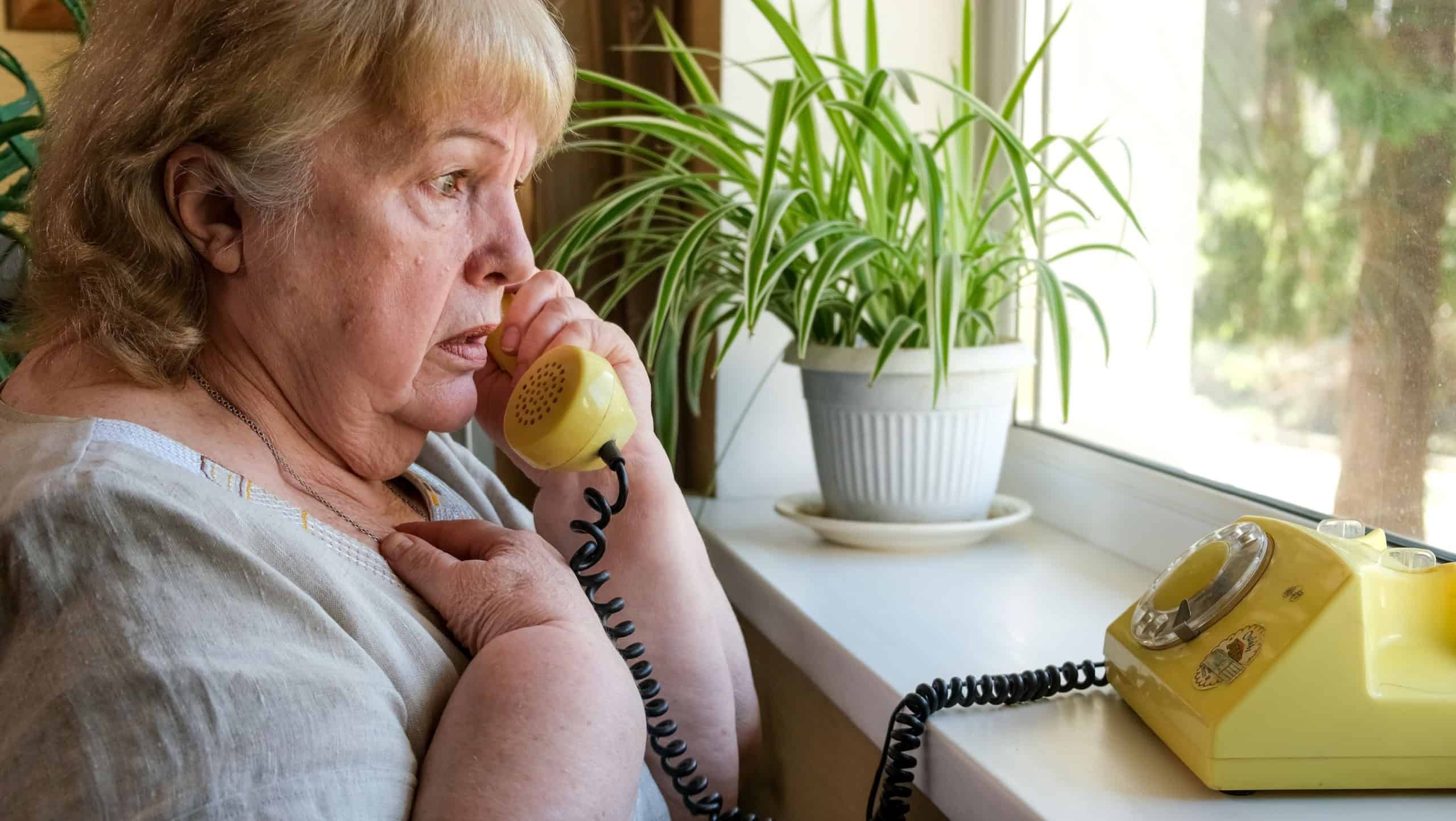 Old woman receives phone call from a scammer. Frightened grandmother talking on an old disc phone
