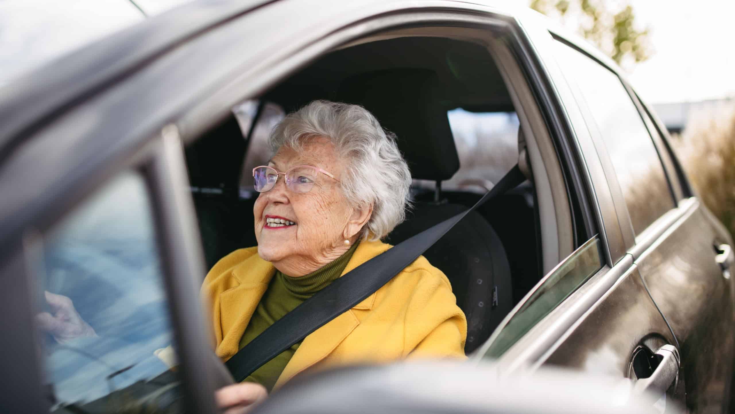 Happy senior woman driving car alone, enjoying car ride. Safe driving for elderly adults, older driver safety.