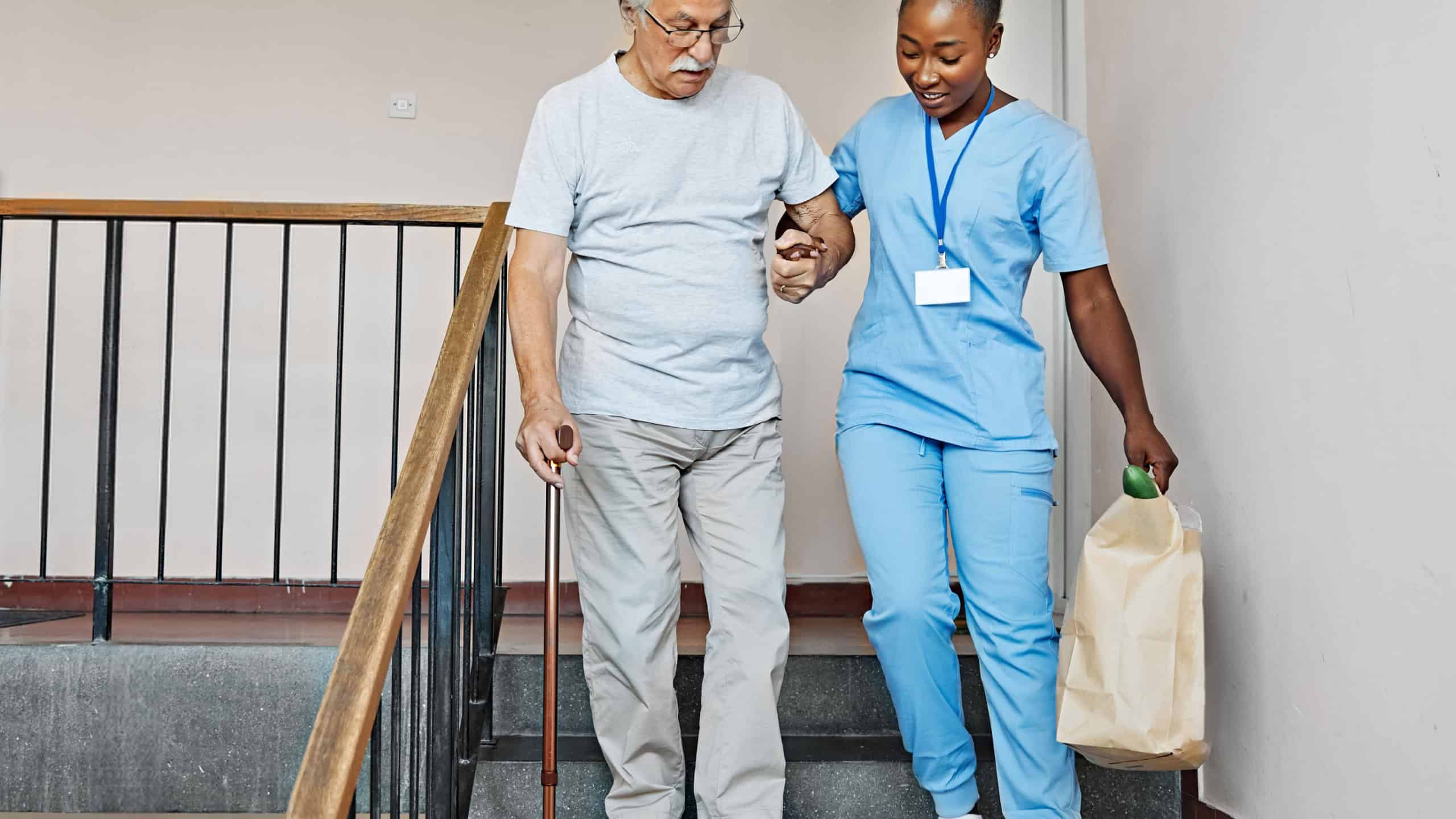 Doctor or nurse caregiver helping disabled senior man walking down the stairs at home or nursing home