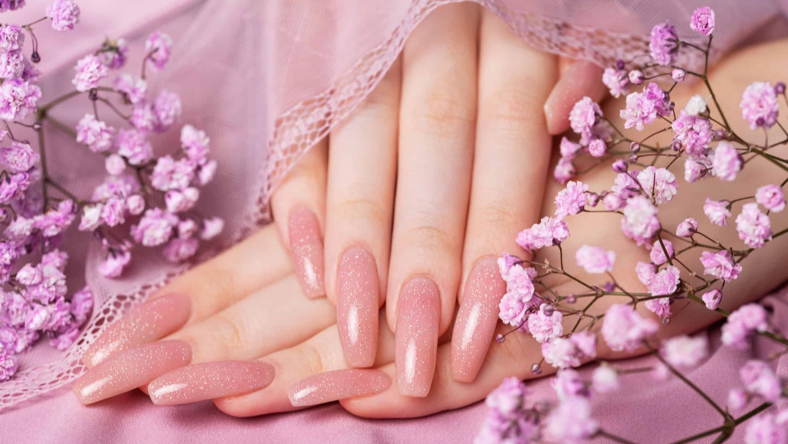 Female hands with pink nail design hold gypsophila flowers. Pink nail polish manicure on pink background