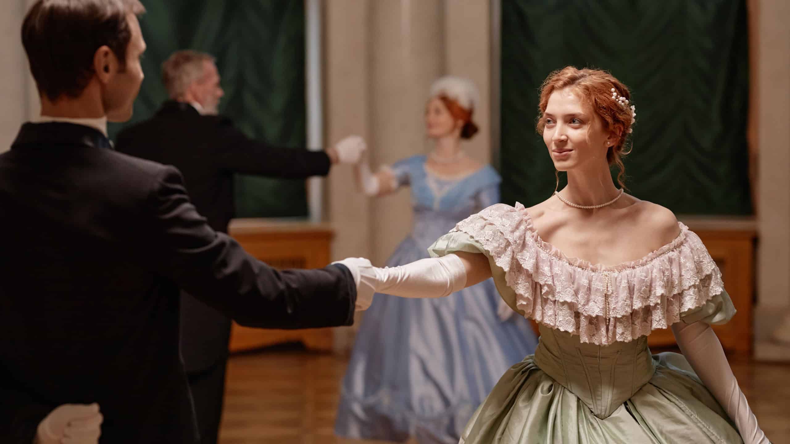 Side view portrait of beautiful young lady dancing with gentleman partner in palace ballroom