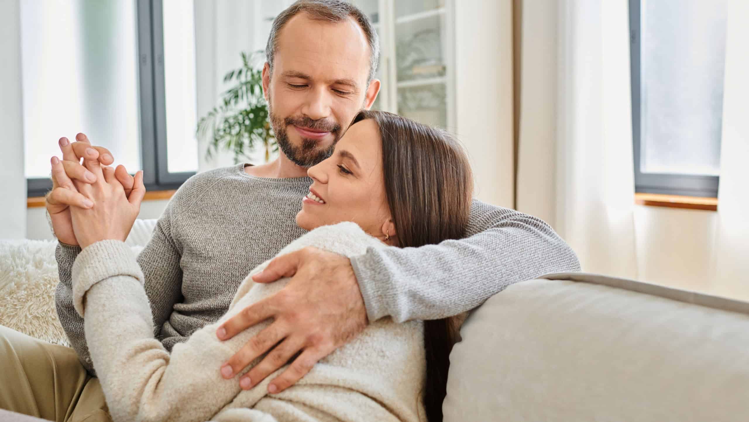 pleased child-free couple holding hands and embracing at home in living room, warm relationship