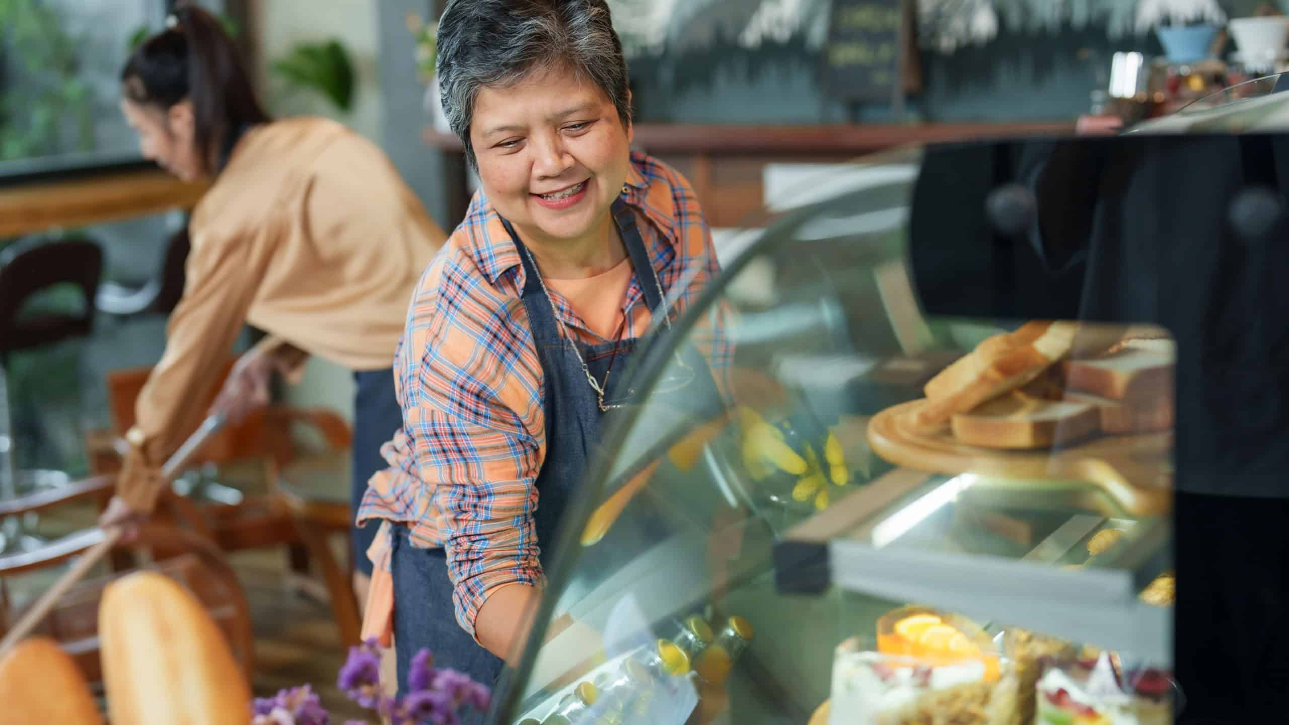 Businessman, owner of small cafe, gray-haired woman, senior citizen, retiree, pensioner, single mother Cleaning the bread and bakery cabinet glass. and the daughter was mopping the floor in the back.