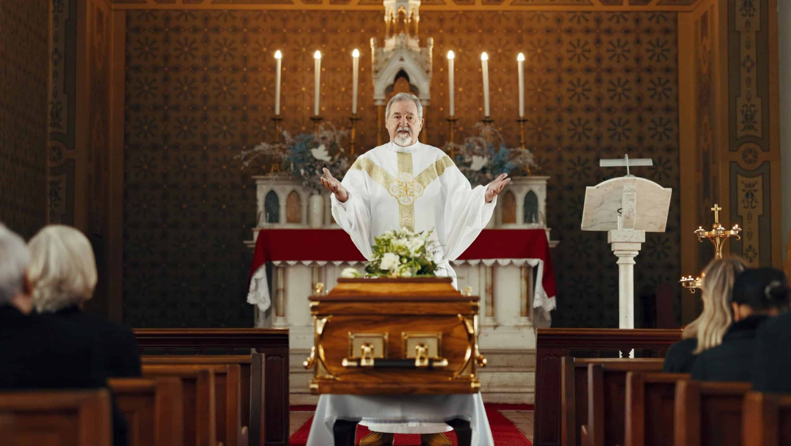 Funeral, church and pastor with prayer by coffin for memorial service, sermon and ceremony for death. Religion, guidance and male priest praying with congregation for comfort with casket in chapel