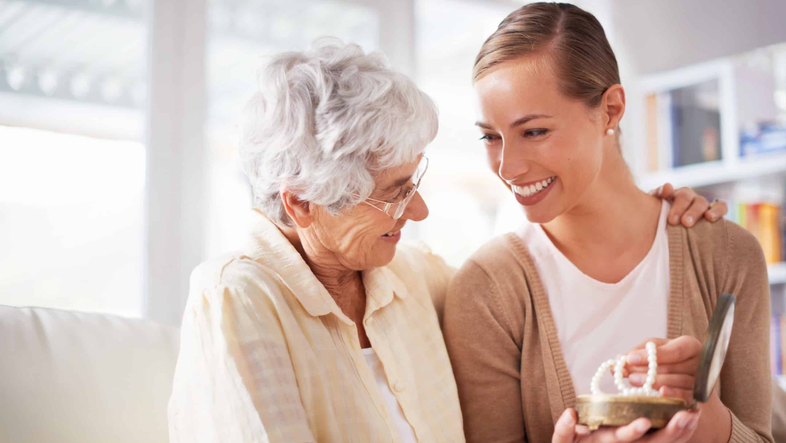 Happy, necklace and senior mother with woman for gift, present and surprise in living room. Family, love and daughter with mom giving pearls on sofa for celebration, birthday and bonding in home