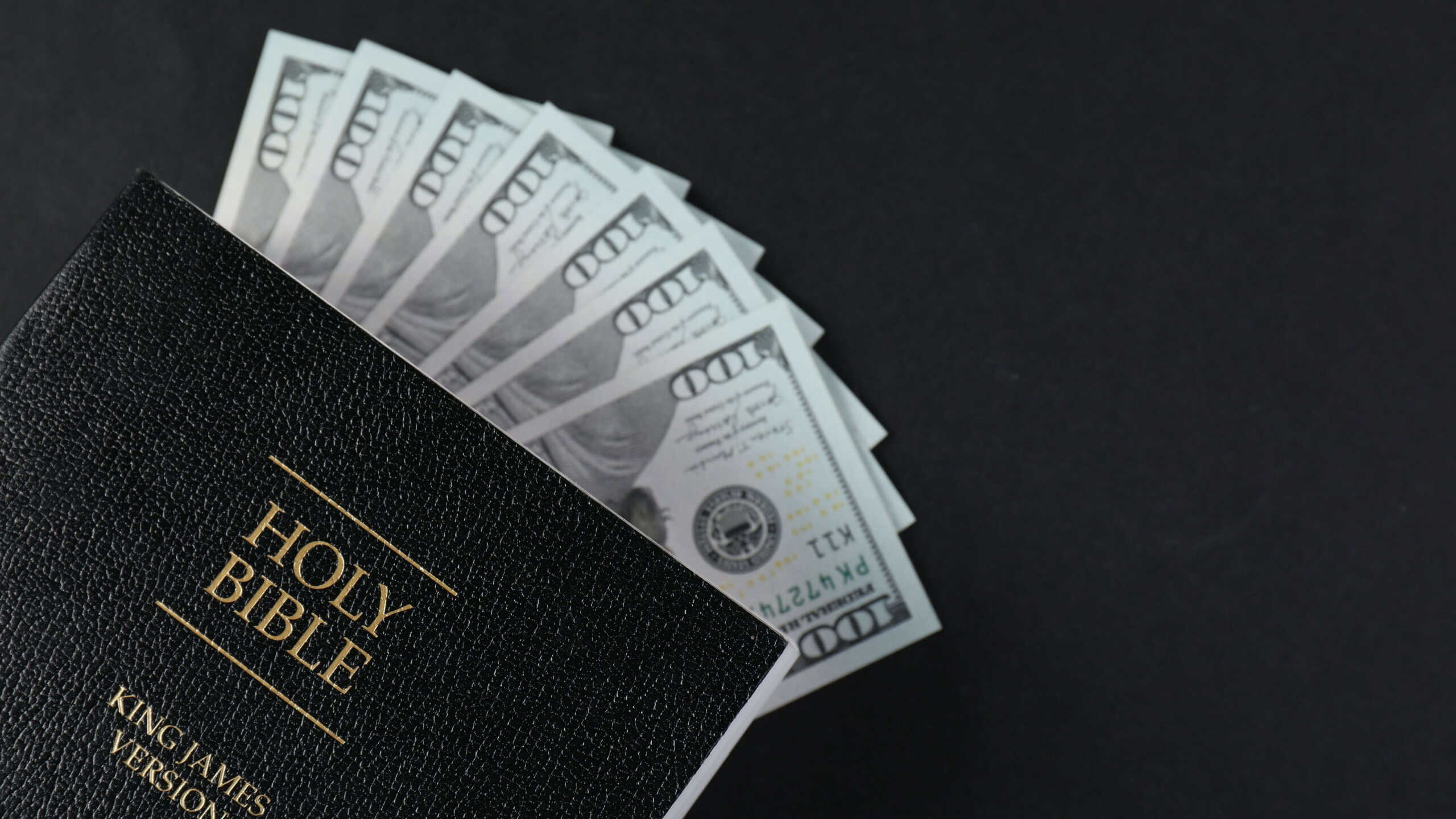 Holy Bible with money on black background, top view