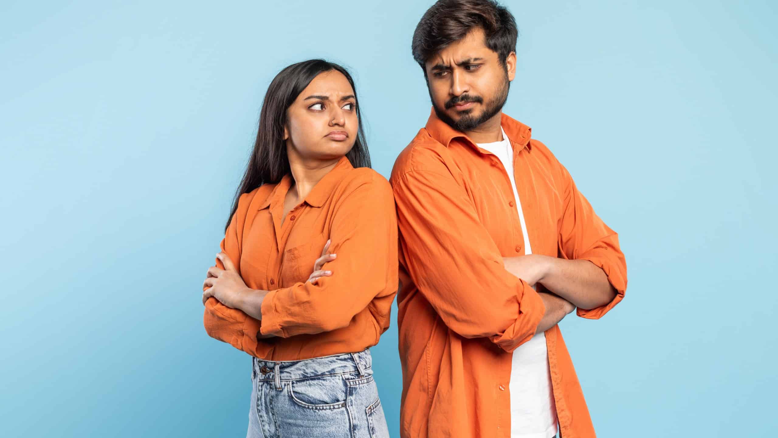 Indian man and woman facing away from each other with crossed arms, signaling a disagreement, against blue background