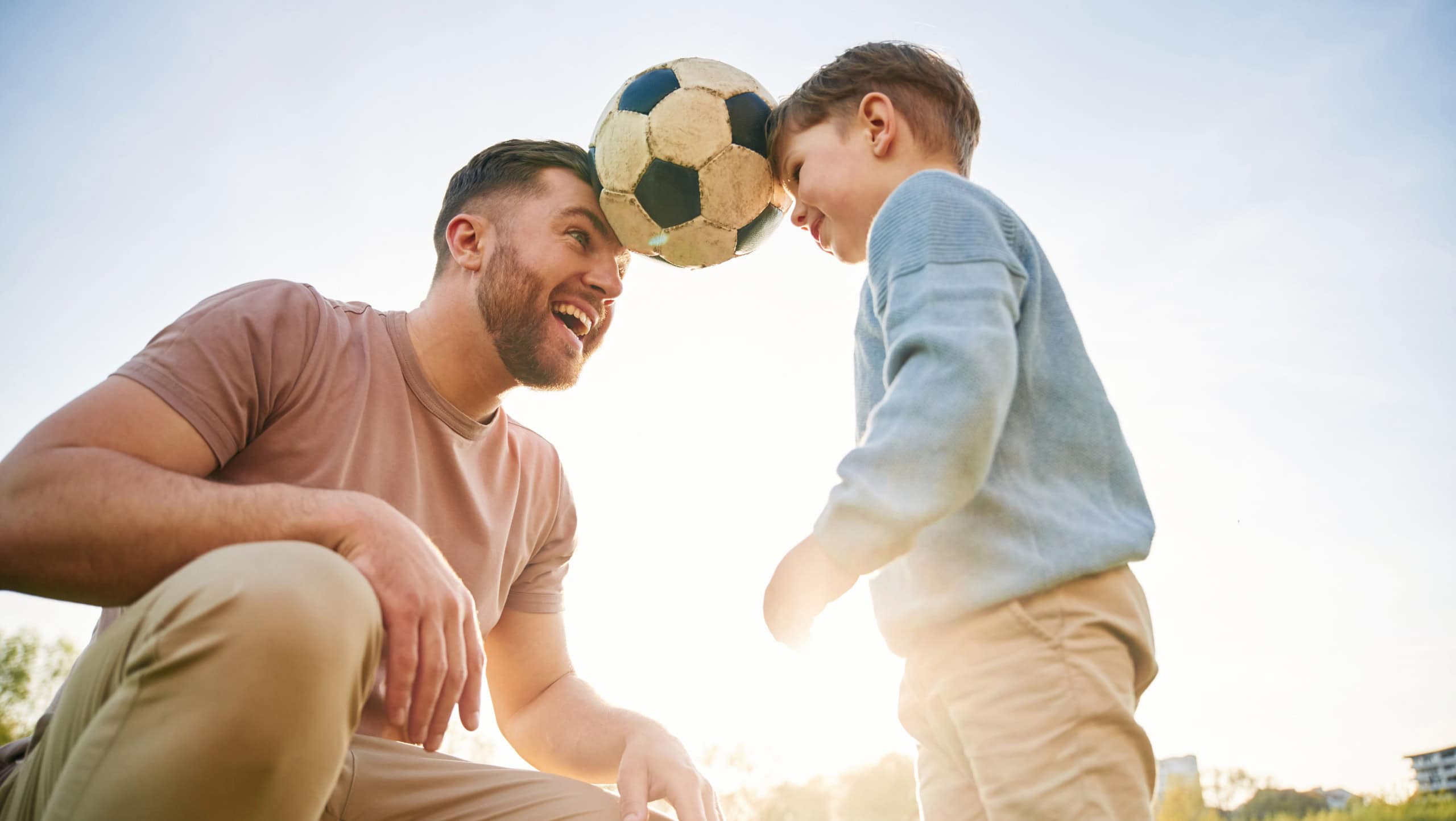 Soccer ball, holding it by heads, fun. Happy father with son are on the field at summertime.