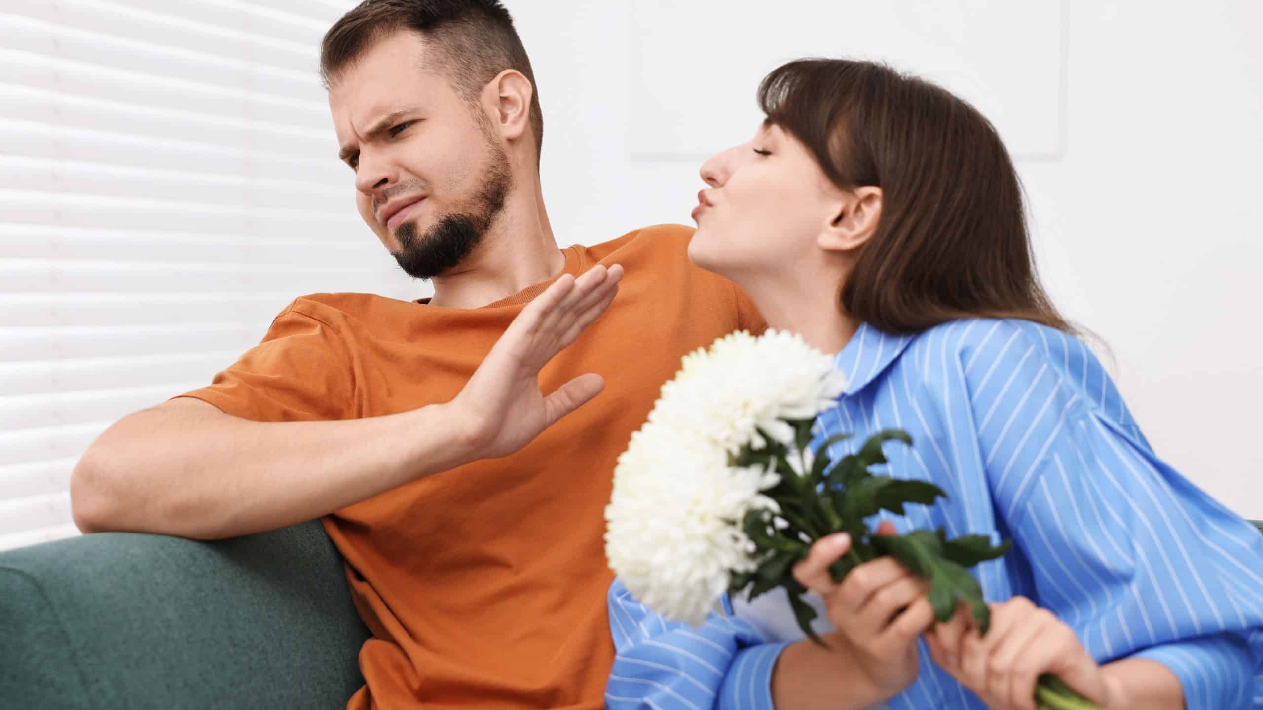 Embarrassed man refusing from woman's kiss at home