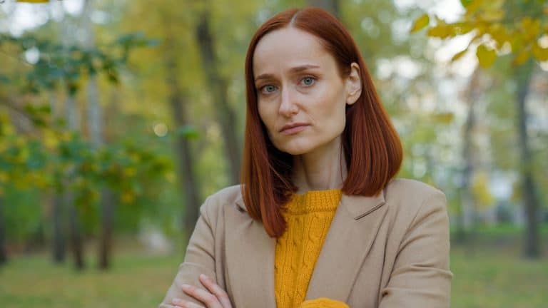 Serious offended Caucasian woman in autumn park in city outdoors posing confident alone looking at camera angry sad upset girl lady crossed hands on chest stressed female in fall season crossing arms