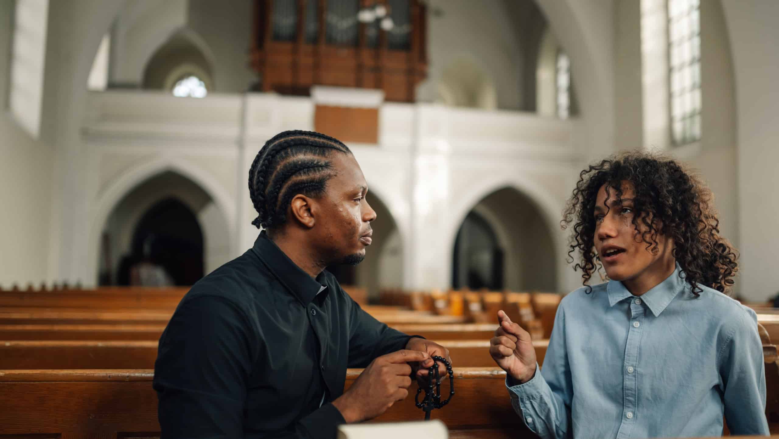 Priest listens to a young man's problems, offering support and guidance in a church setting. The image conveys faith, hope, and compassion
