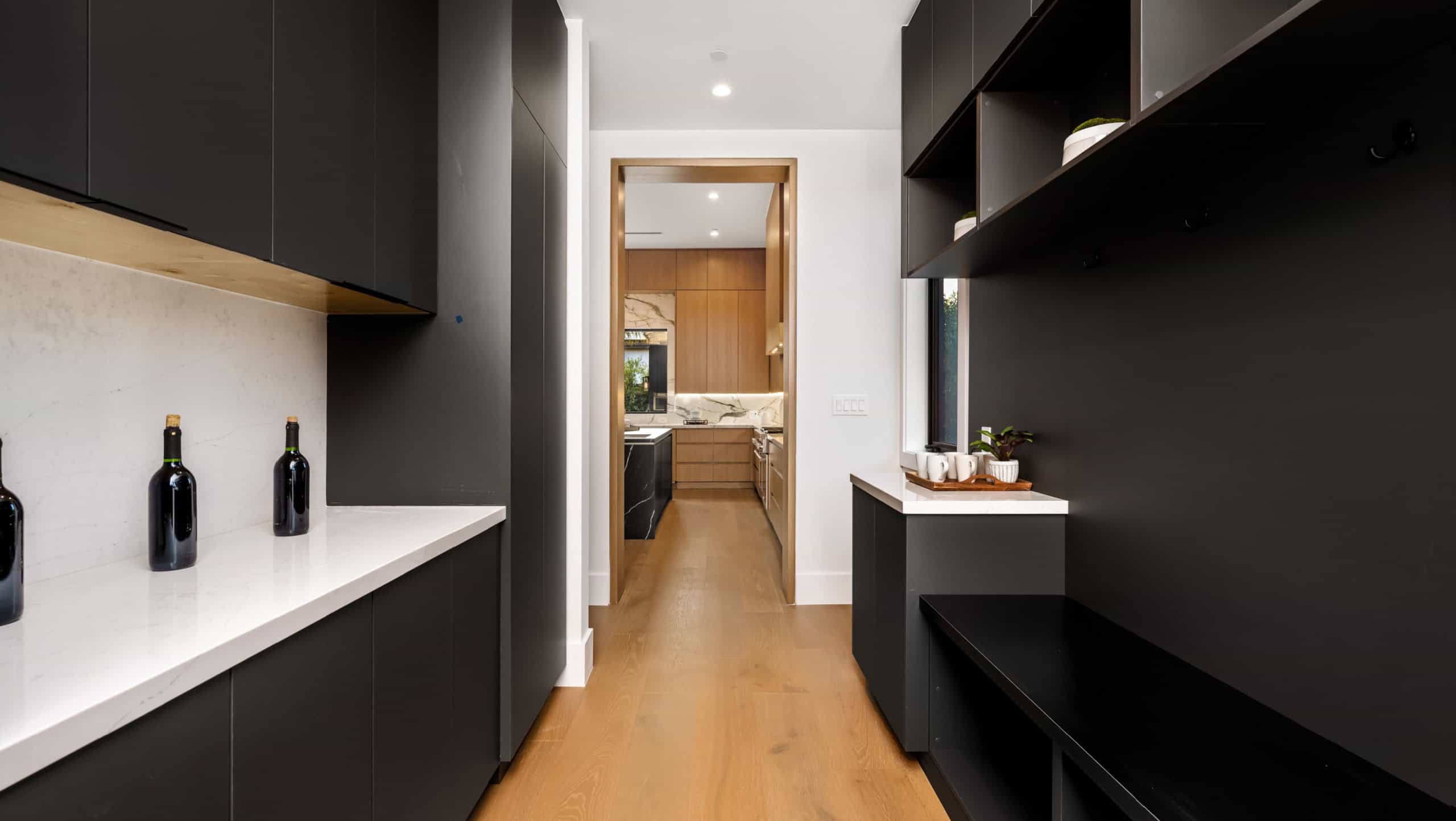 Modern kitchen interior with black cabinets, white countertops, and wooden flooring leading to a dining area.