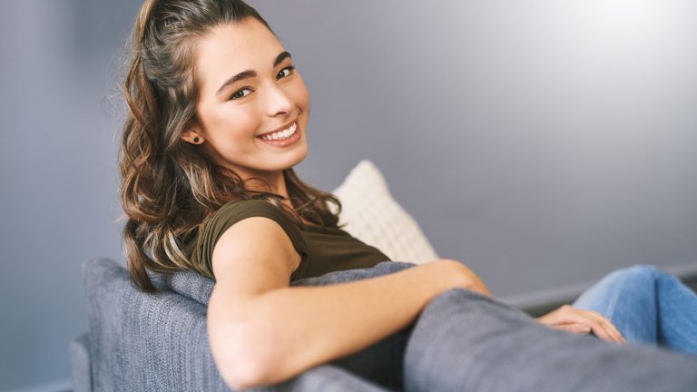 Happy, home and portrait of woman on sofa for resting, relaxing and comfortable on weekend. Apartment, living room and person on couch for chilling, break and calm with confidence, pride and smile