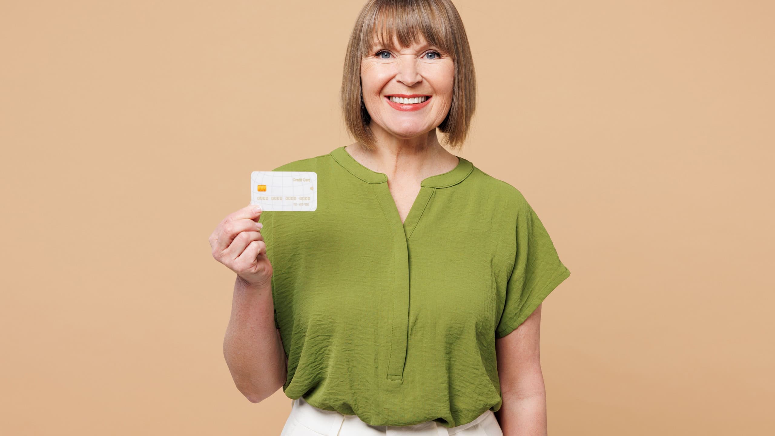 Elderly happy blonde woman 50s years old she wear green shirt casual clothes hold in hand mock up of credit bank card isolated on plain pastel light beige background studio portrait. Lifestyle concept