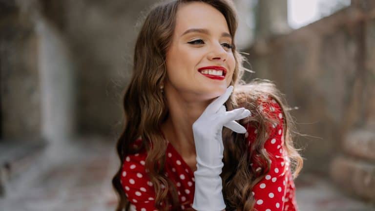 Beautiful pin-up girl in red polka dot dress and white gloves smiling and posing in an old building