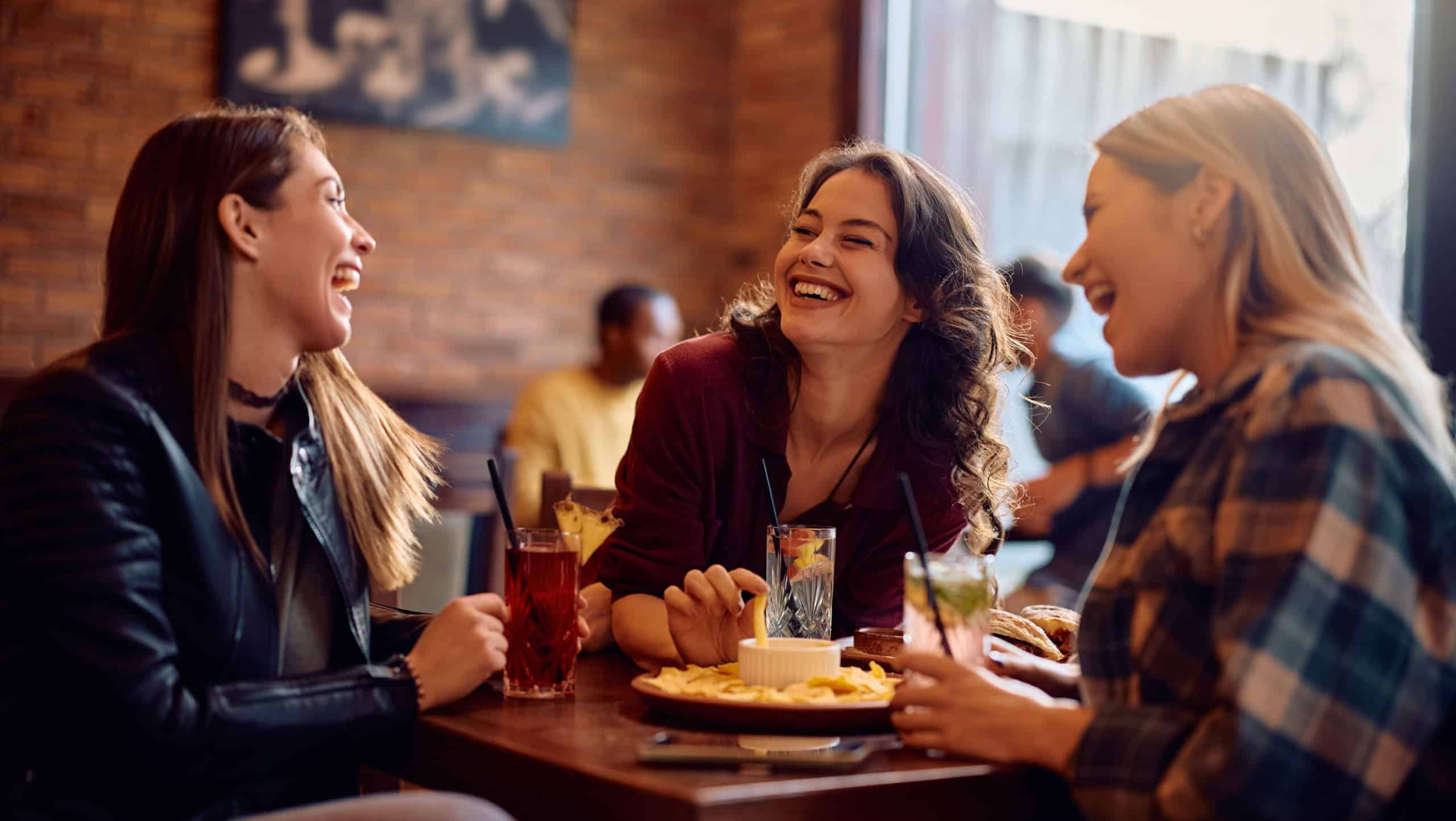 Young happy women laughing while drinking and talking in a pub.
