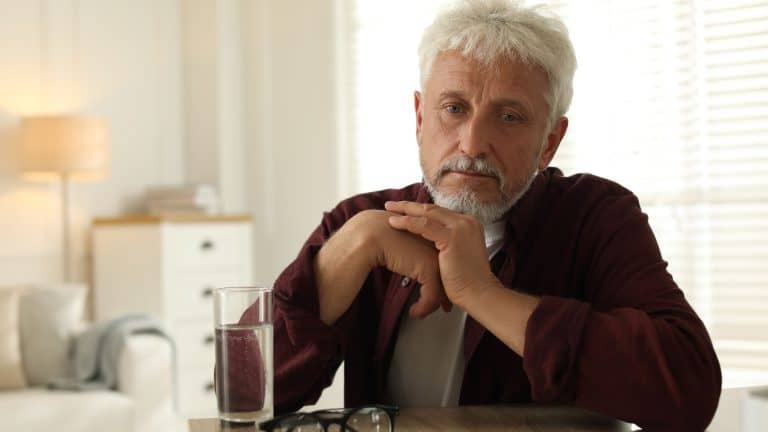 Sad senior man feeling lonely while sitting at wooden table indoors
