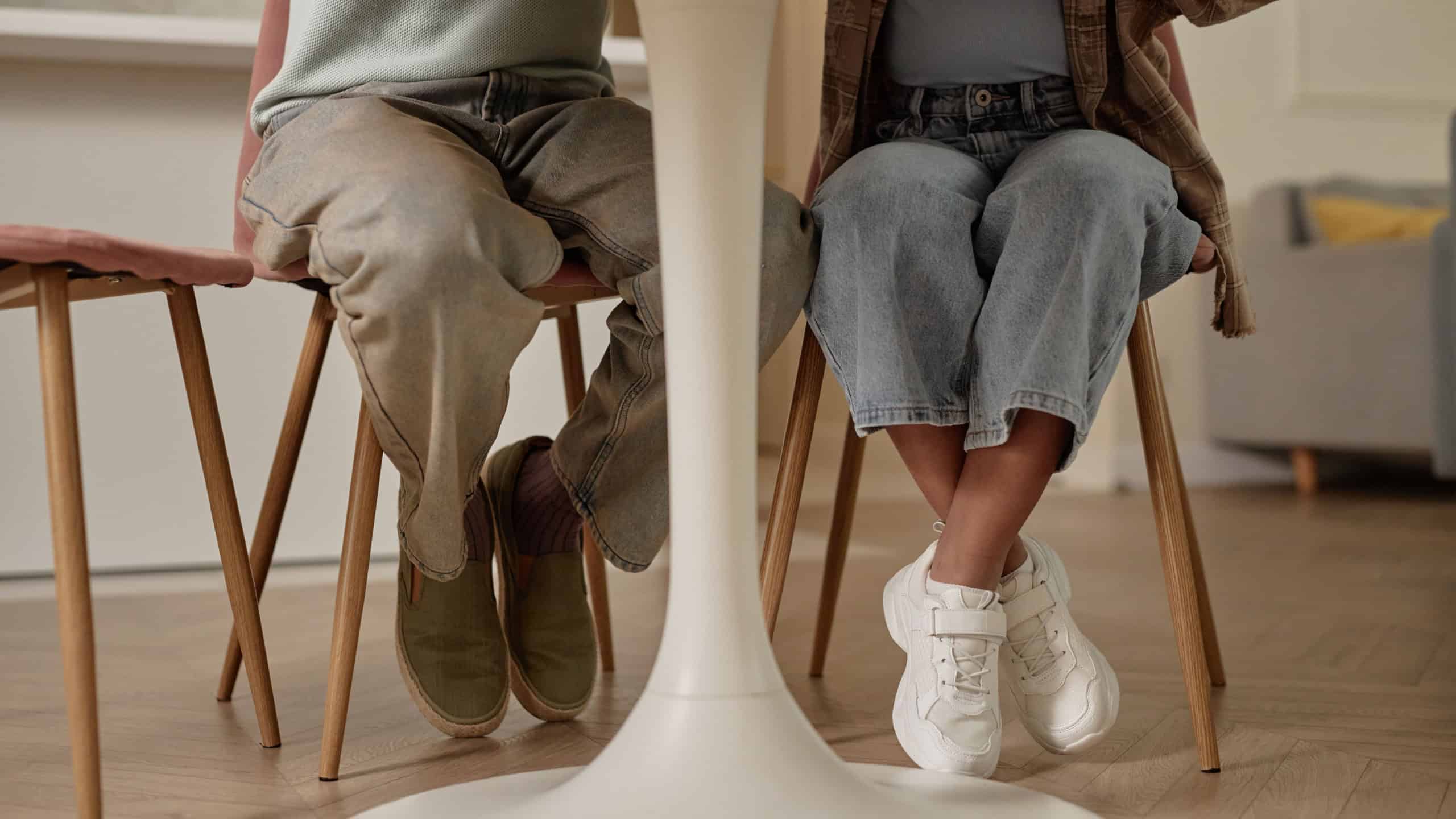 Cropped shot of legs of African American father and daughter sitting at table in kitchen spending time together at home