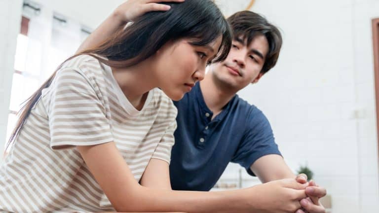 Asian young husband comforting his wife crying with tears for problem. Attractive man support, consoling and understand empathy to depressed stressed woman in bedroom at home. Family relationship.