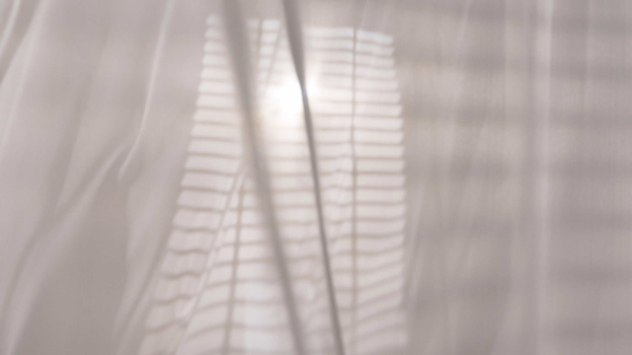 Transparent white silk curtains in daylight floating from an open window, shadows from window blinds reflected on the textile.