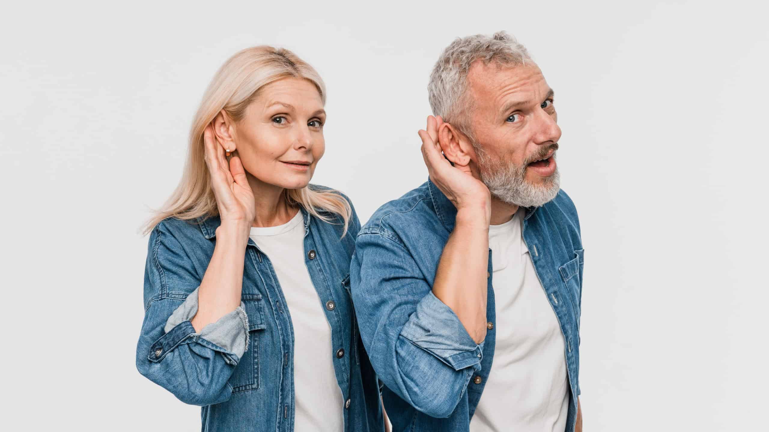 Curious couple two friends elderly gray-haired man blonde woman in denim casual clothes standing try to hear you overhear listening intently isolated on white color background studio portrait
